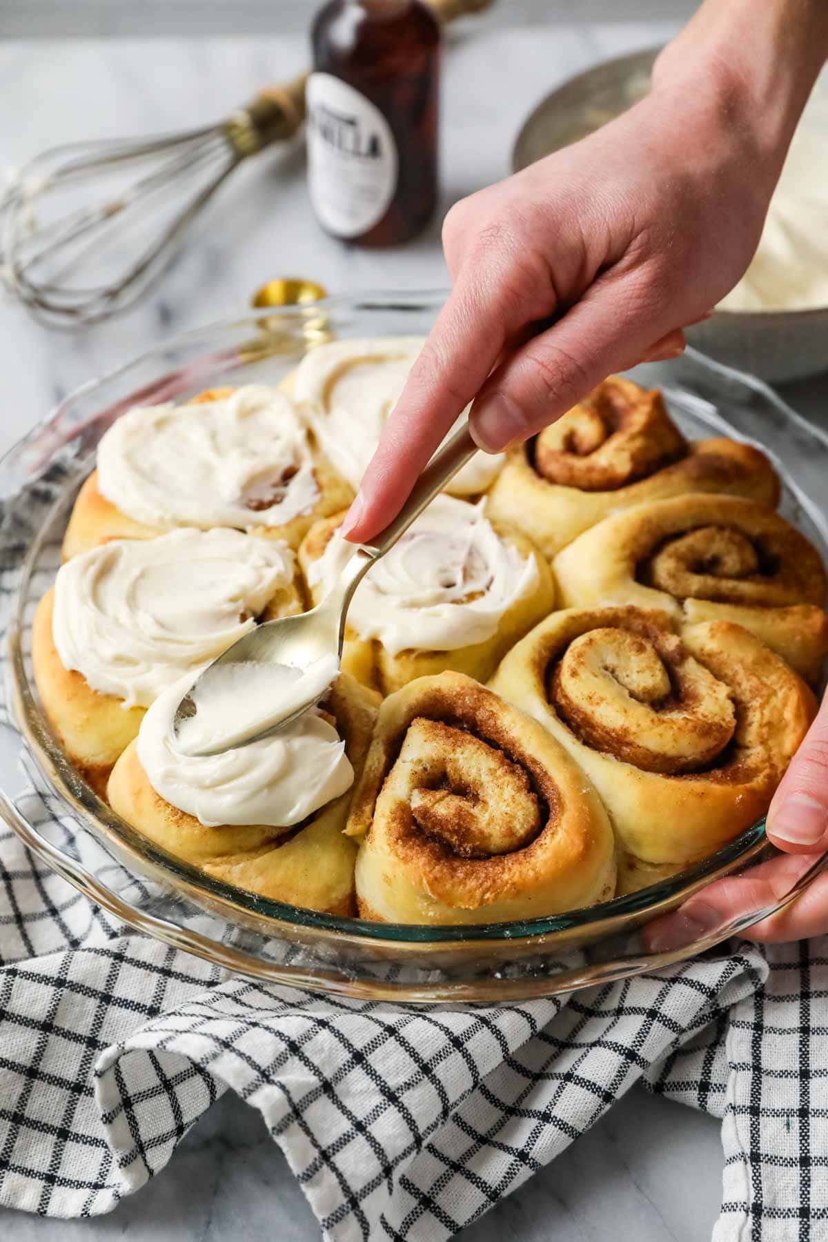Spreading cinnamon roll icing over rolls.