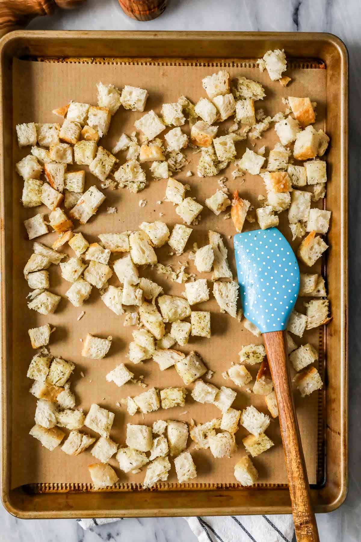 Overhead view of a baking sheet of seasoned croutons before baking.