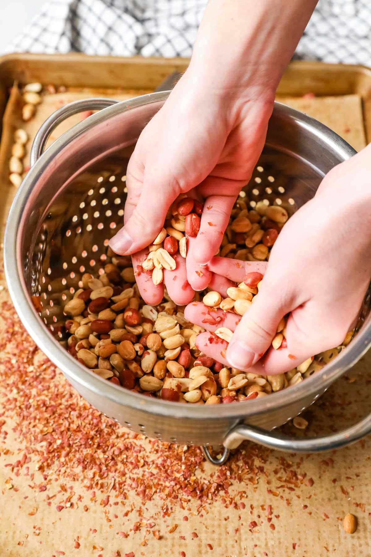 Hands moving peanuts around in a colander to remove the skins.