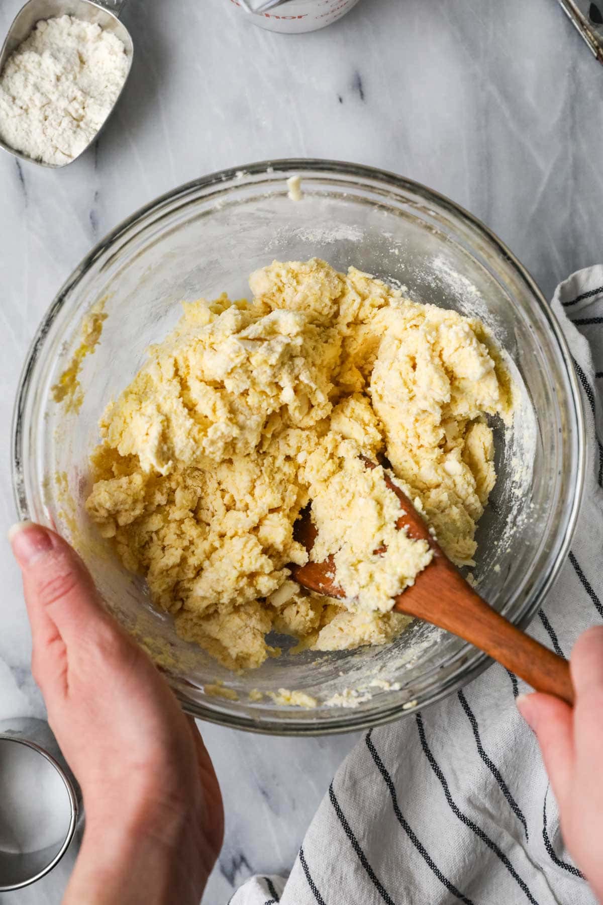Overhead view of a bowl of shaggy biscuit dough made with cornmeal.