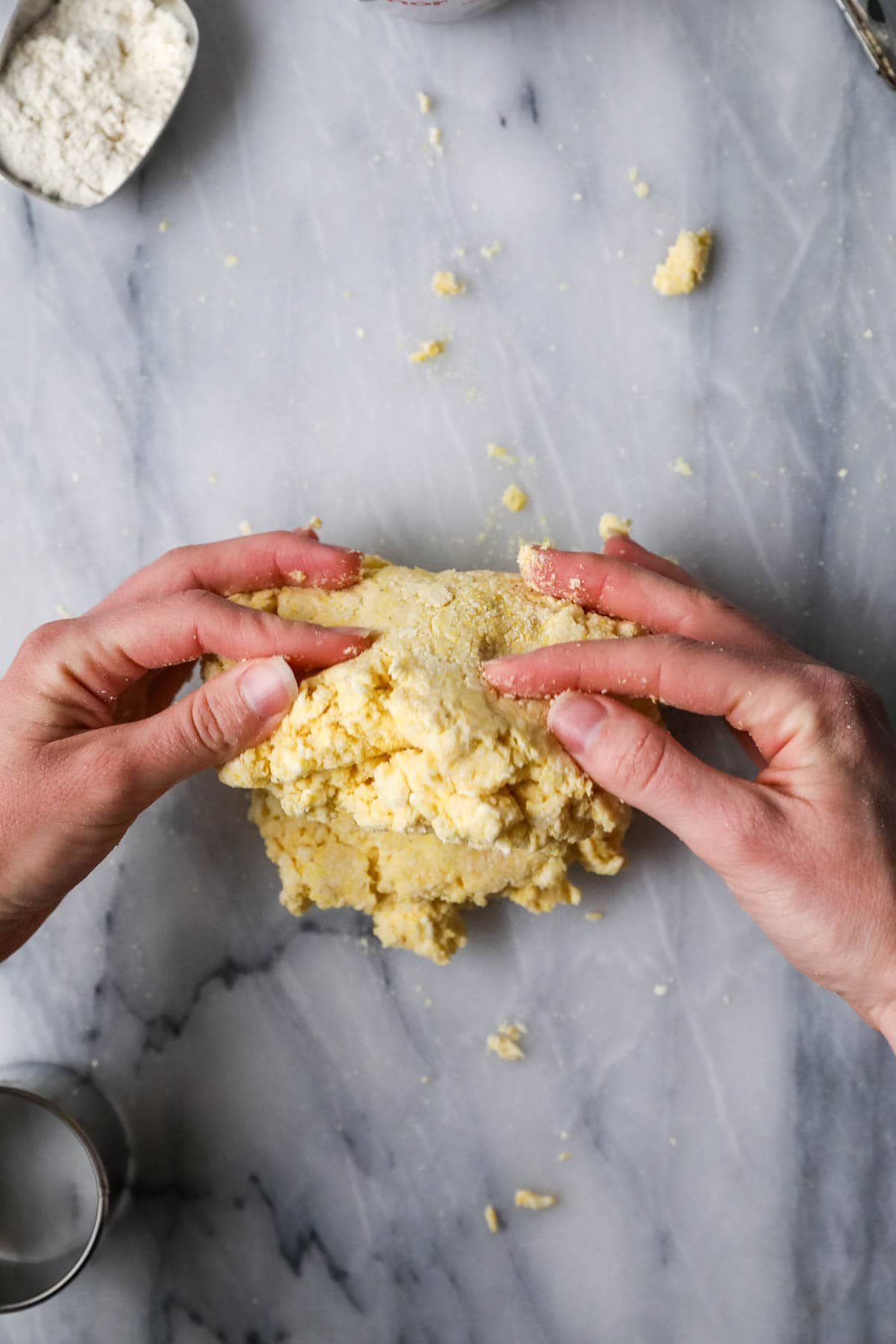 Hands working a shaggy cornmeal biscuit dough together.