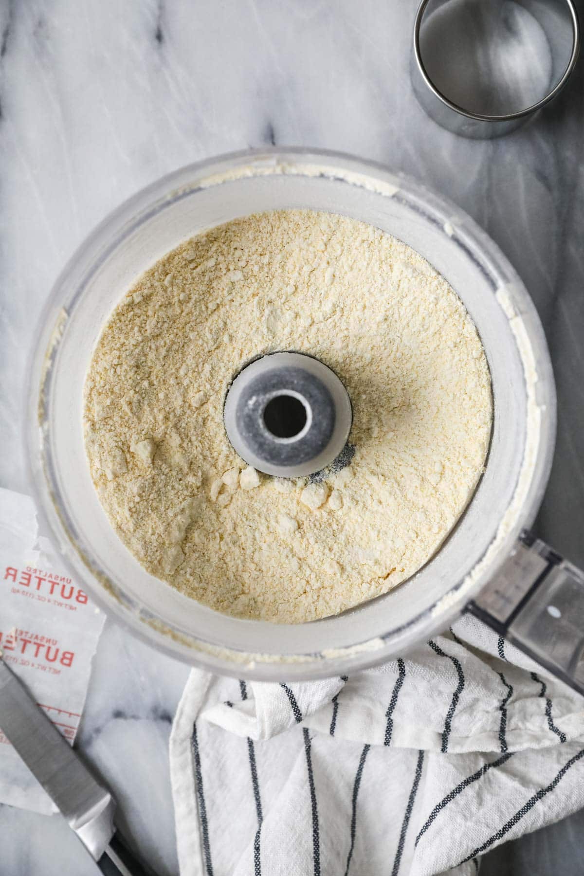 Overhead view of butter being cut into dry ingredients in a food processor.