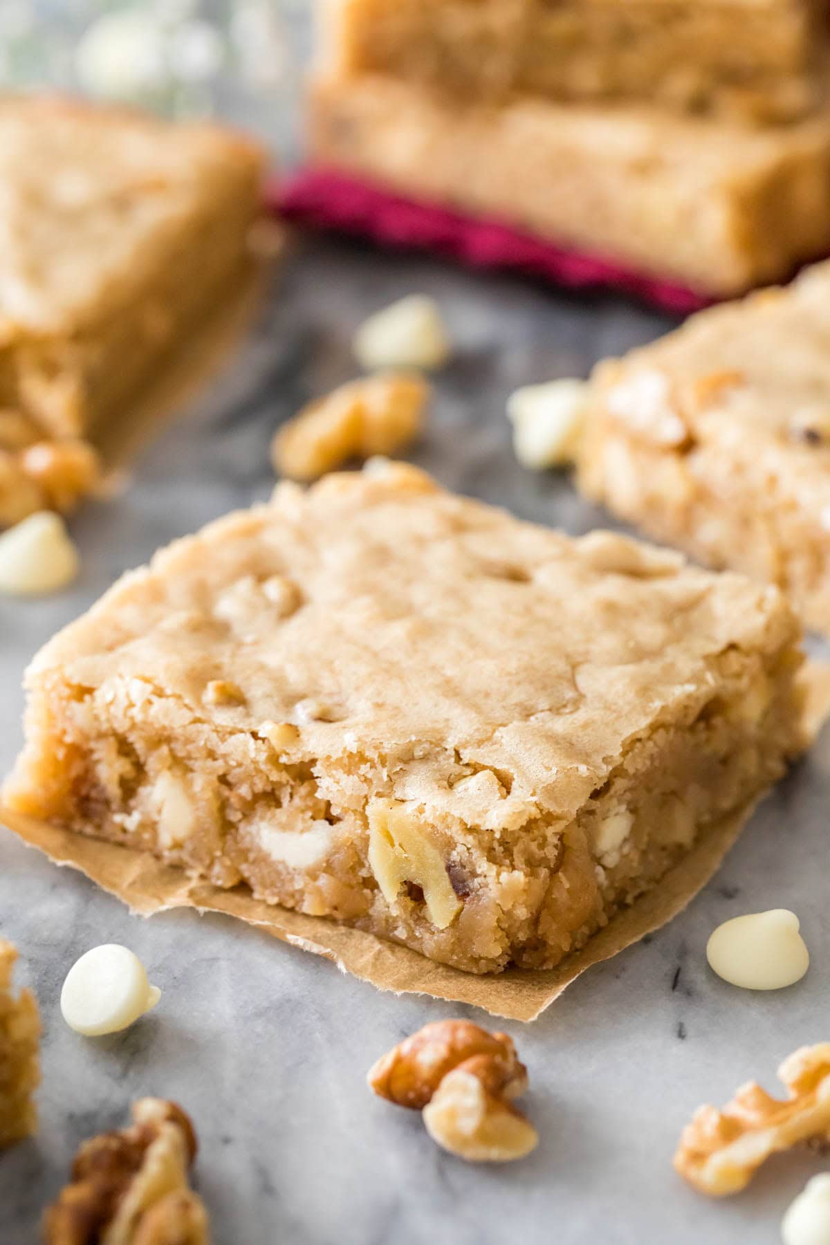 Cut square of blondie on marble, surrounded by more blondies and nuts and white chocolate