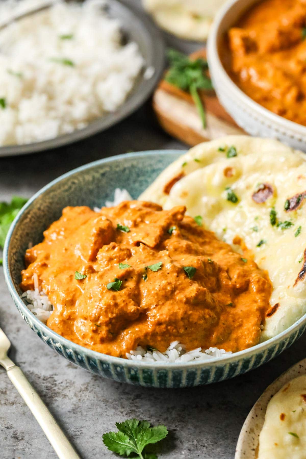 Serving of Indian butter chicken over rice with a piece of naan.