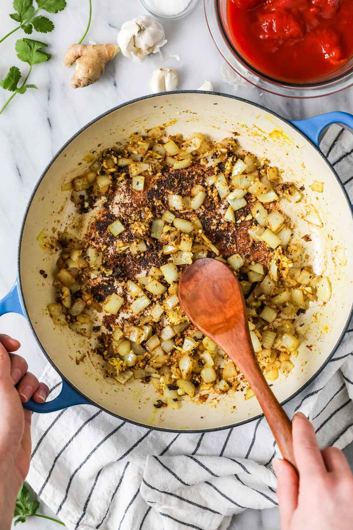 Overhead view of onions, ginger, and garlic sauteing in a large pot.