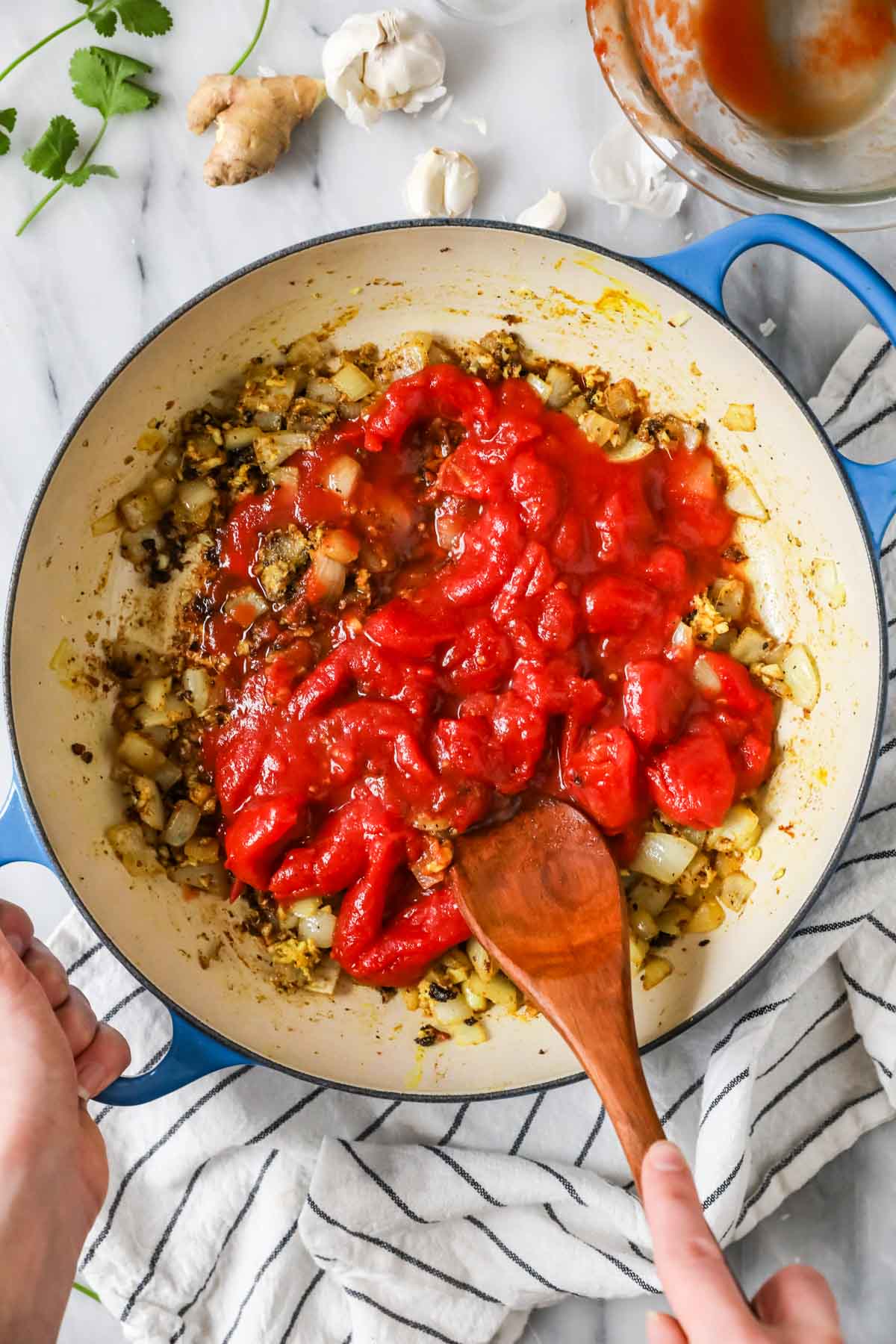 Whole peeled tomatoes being broken up in a large pot.