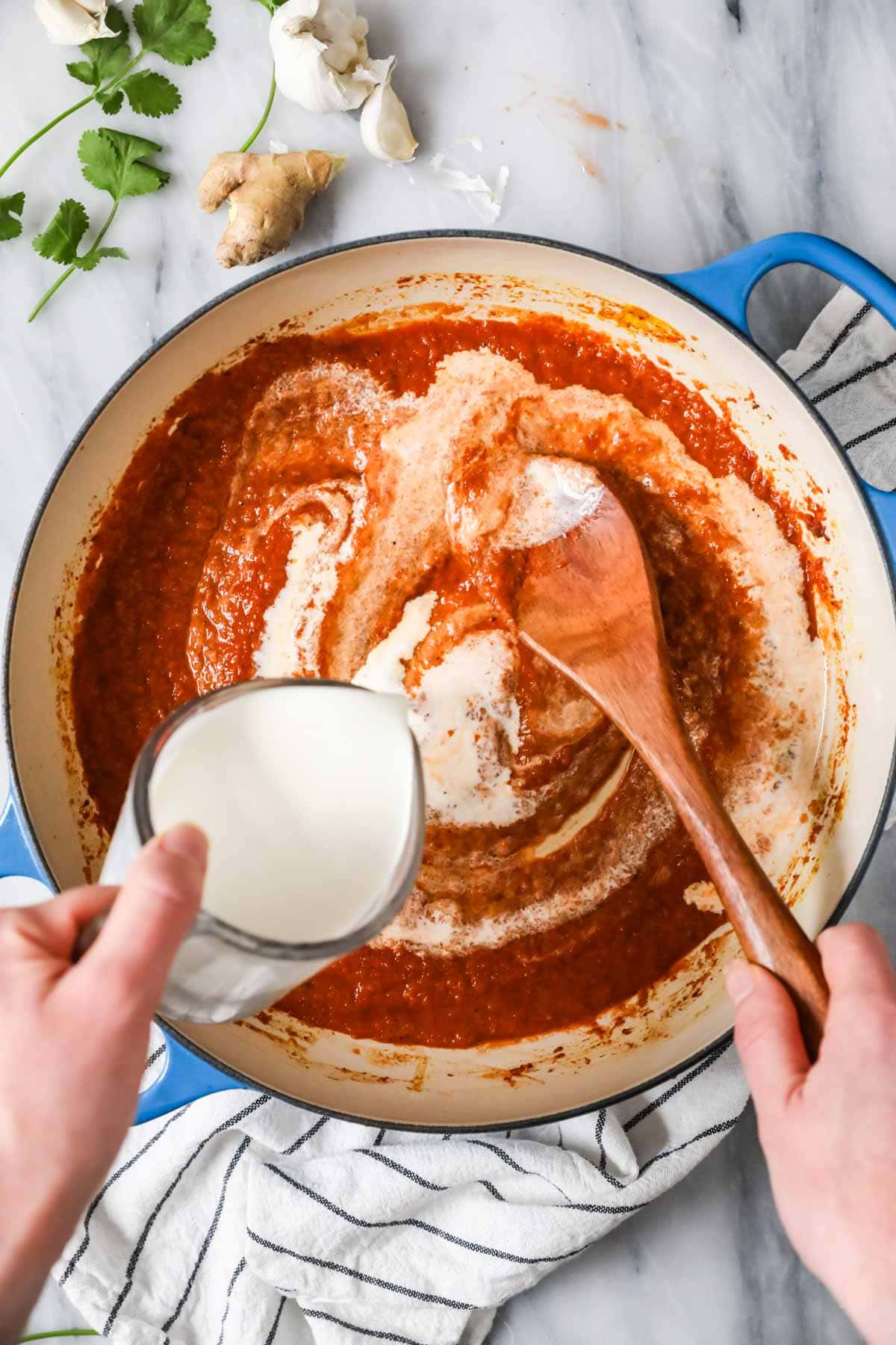 Cream being poured into a butter chicken sauce.