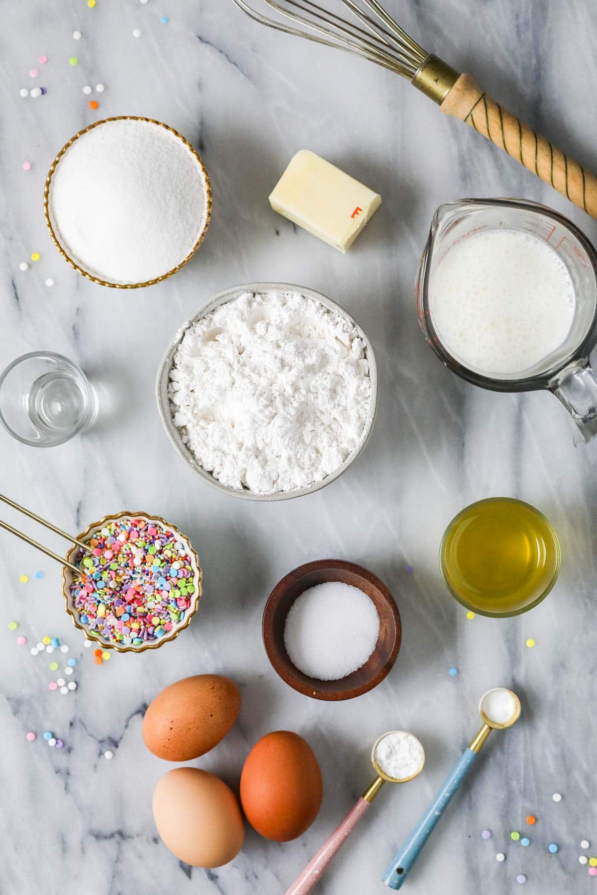 Overhead view of ingredients including sprinkles, cake flour, almond extract, and more.