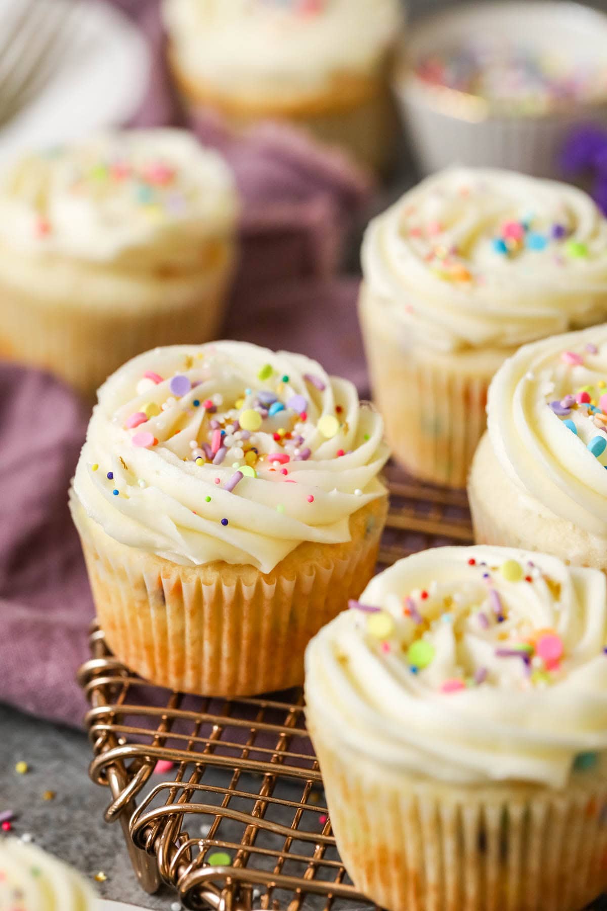 Confetti cupcakes topped with buttercream swirls and sprinkles on a cooling rack.