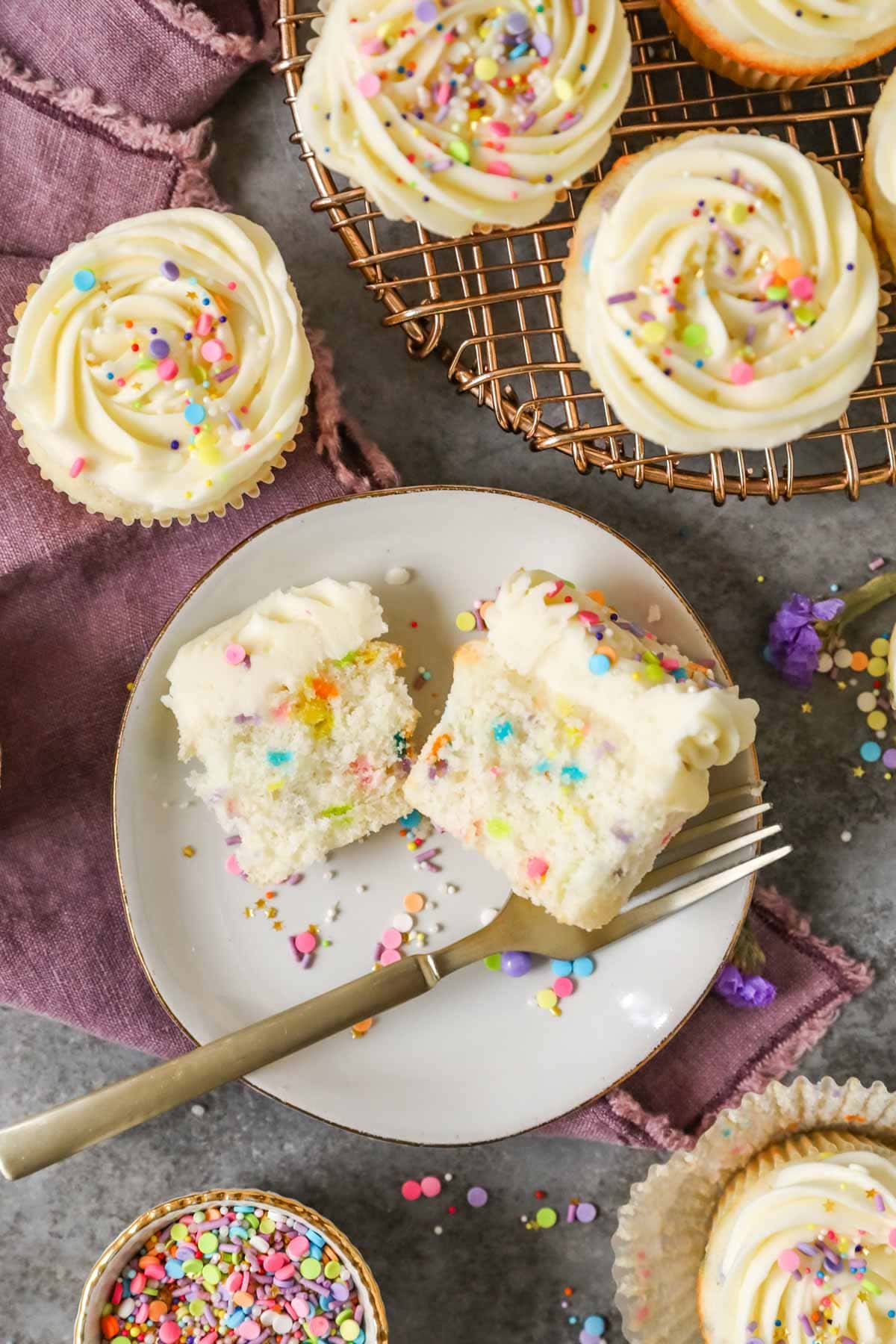 Cupcake that's been cut in half on a plate to show its sprinkle flecked interior.