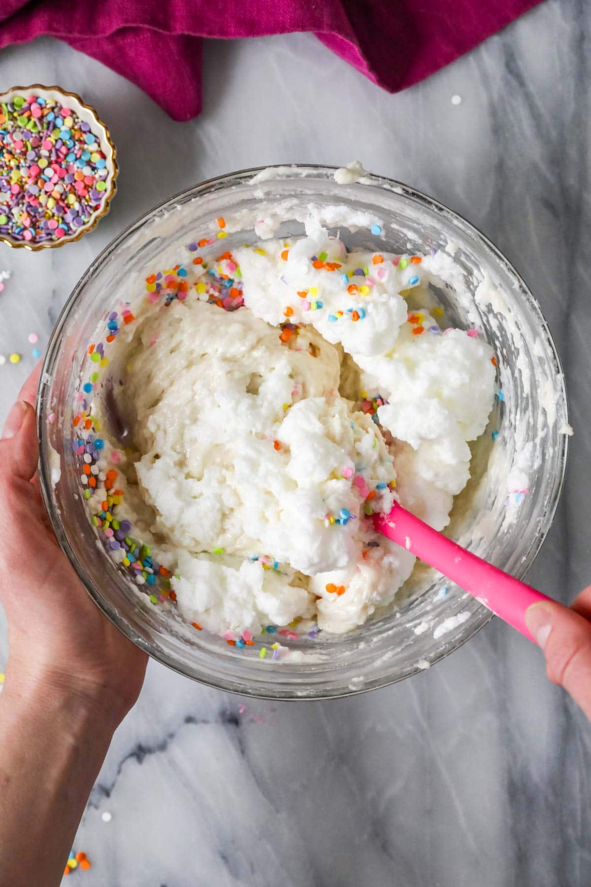 Whipped egg whites and sprinkles being folded into a cupcake batter.