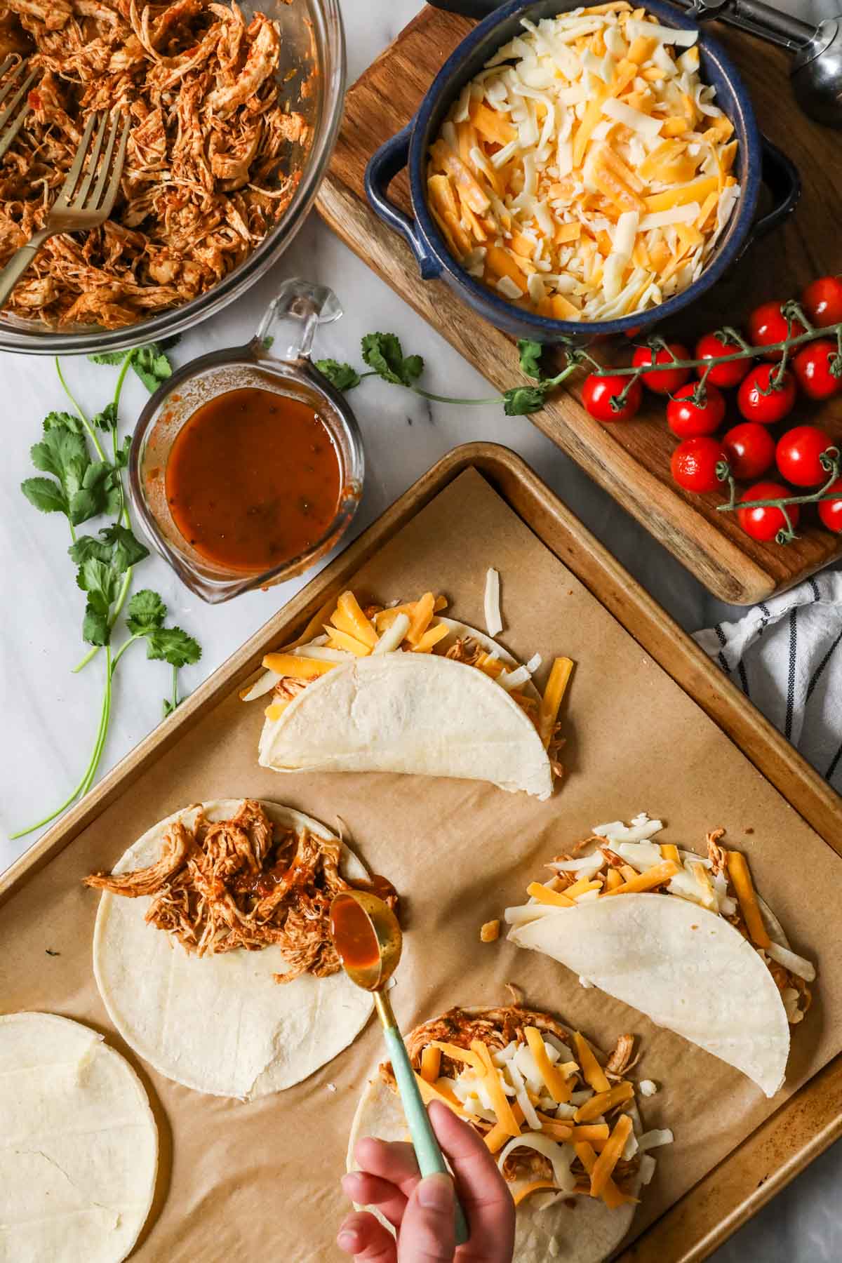 Filling corn tortillas with shredded chicken before topping with cheese.