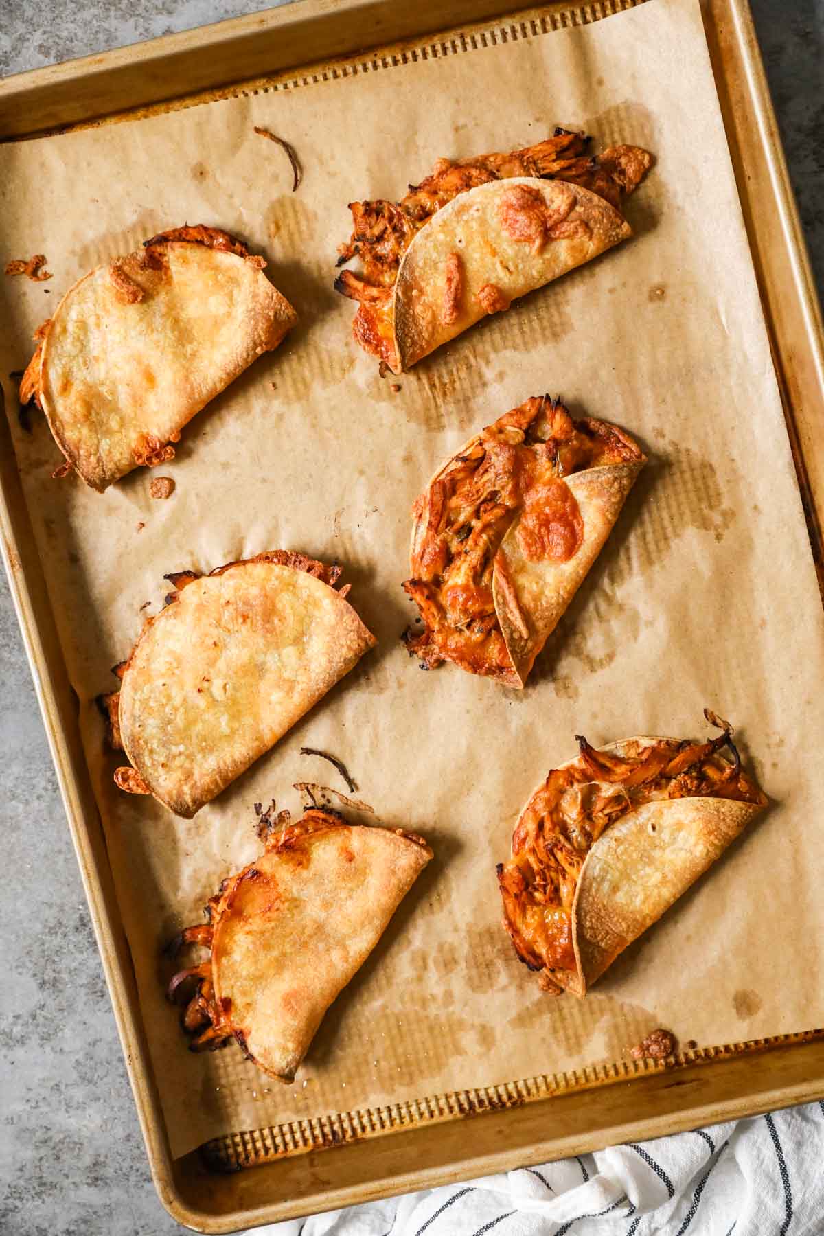 Overhead view of oven baked crispy chicken tacos on a parchment lined baking sheet.