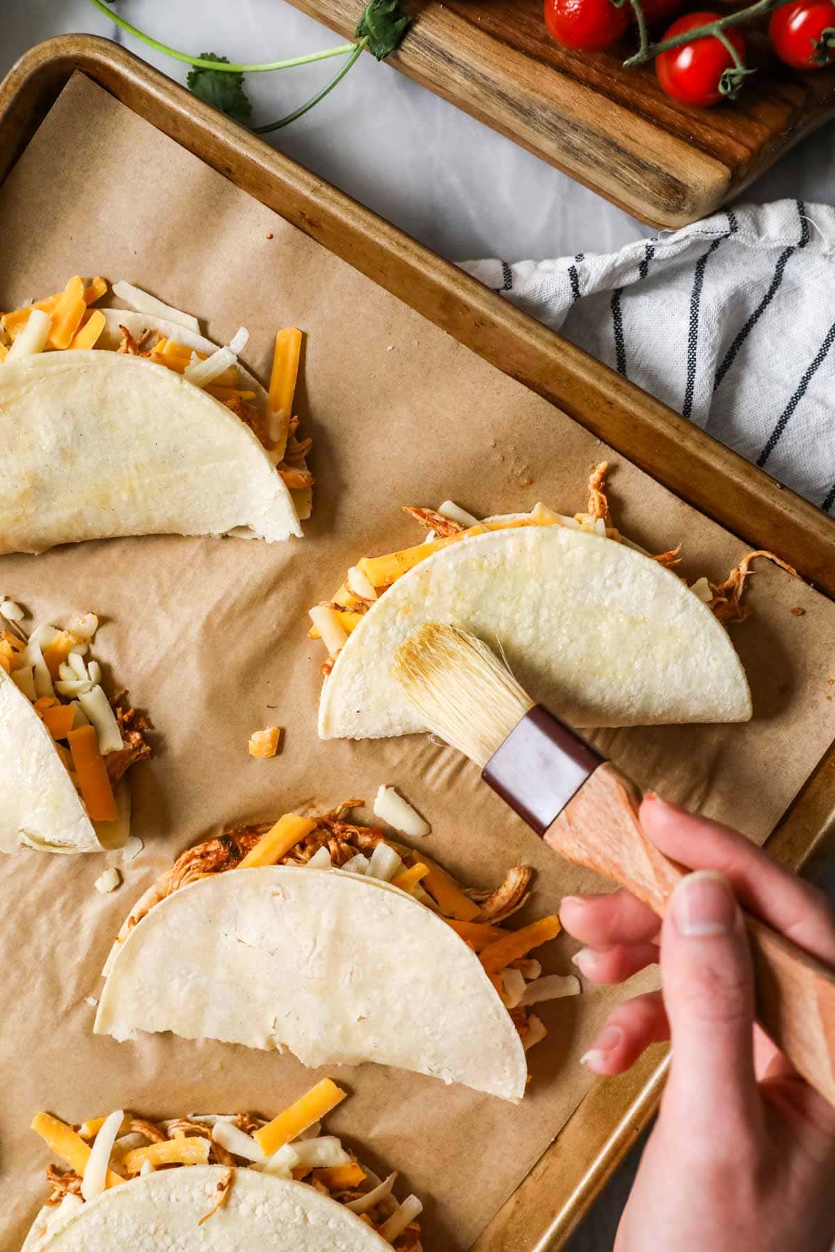 Brushing chicken tacos with oil before baking.
