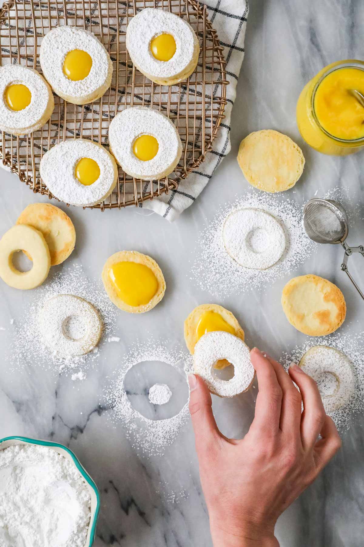 Overhead view of egg cookies being assembled with a lemon curd center and powdered sugar exterior.