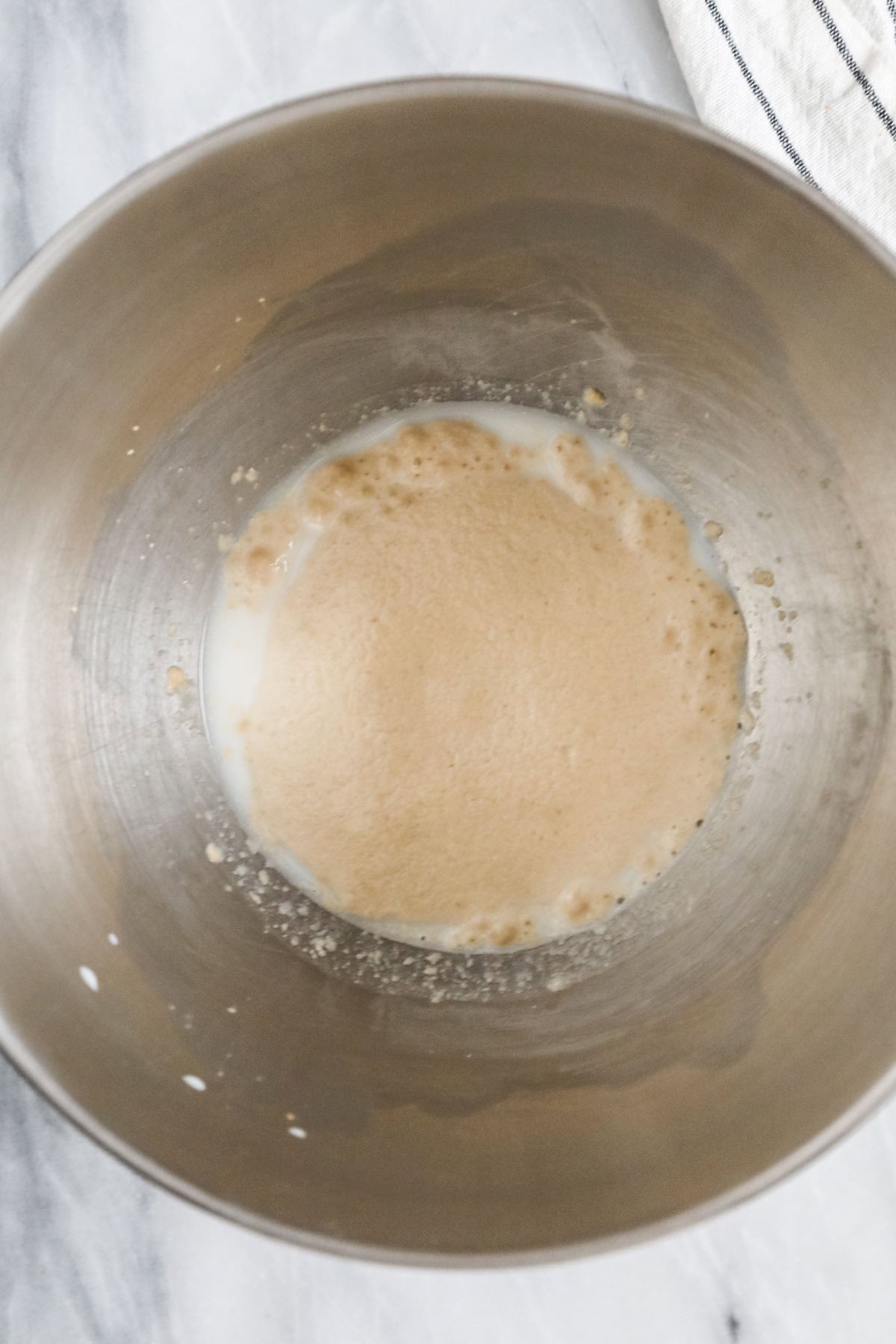 Overhead view of foamy yeast in the bottom of a metal bowl.