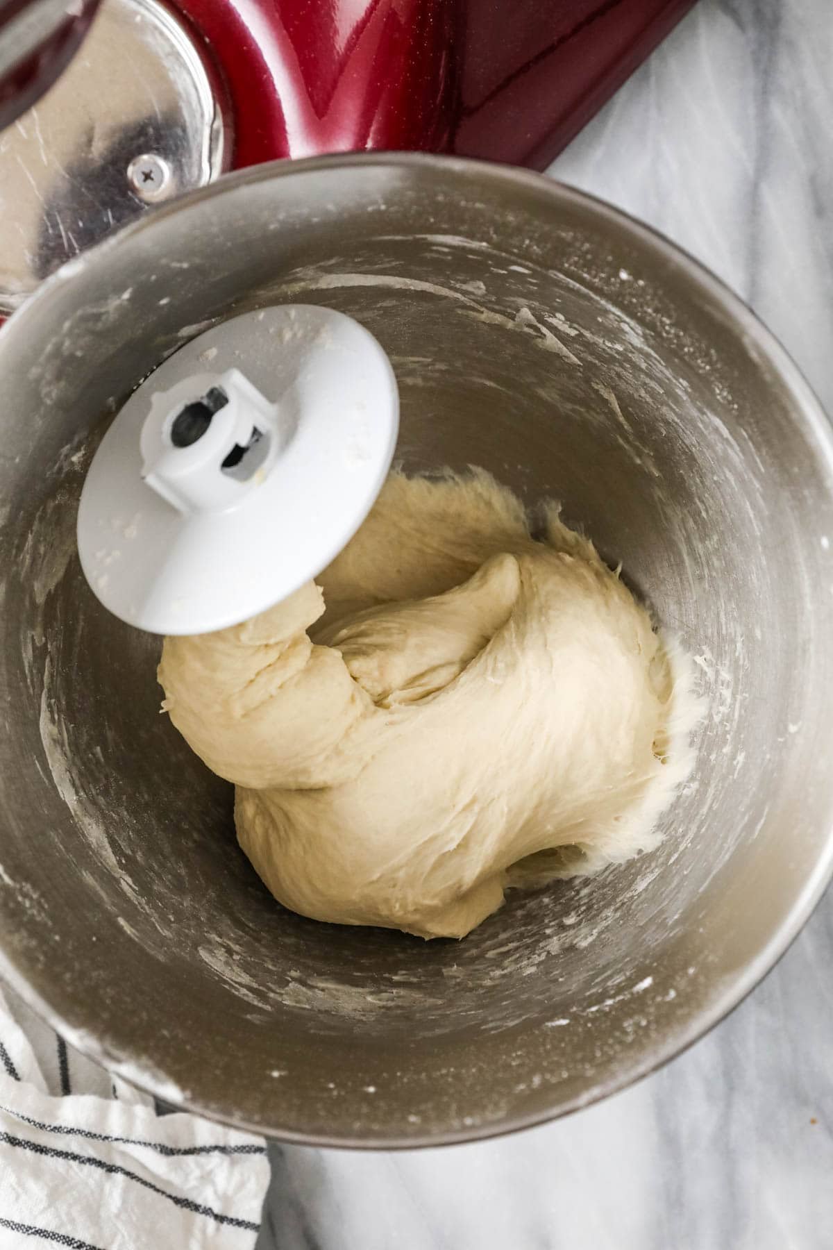 Overhead view of dough clinging to a dough hook in a stand mixer bowl.
