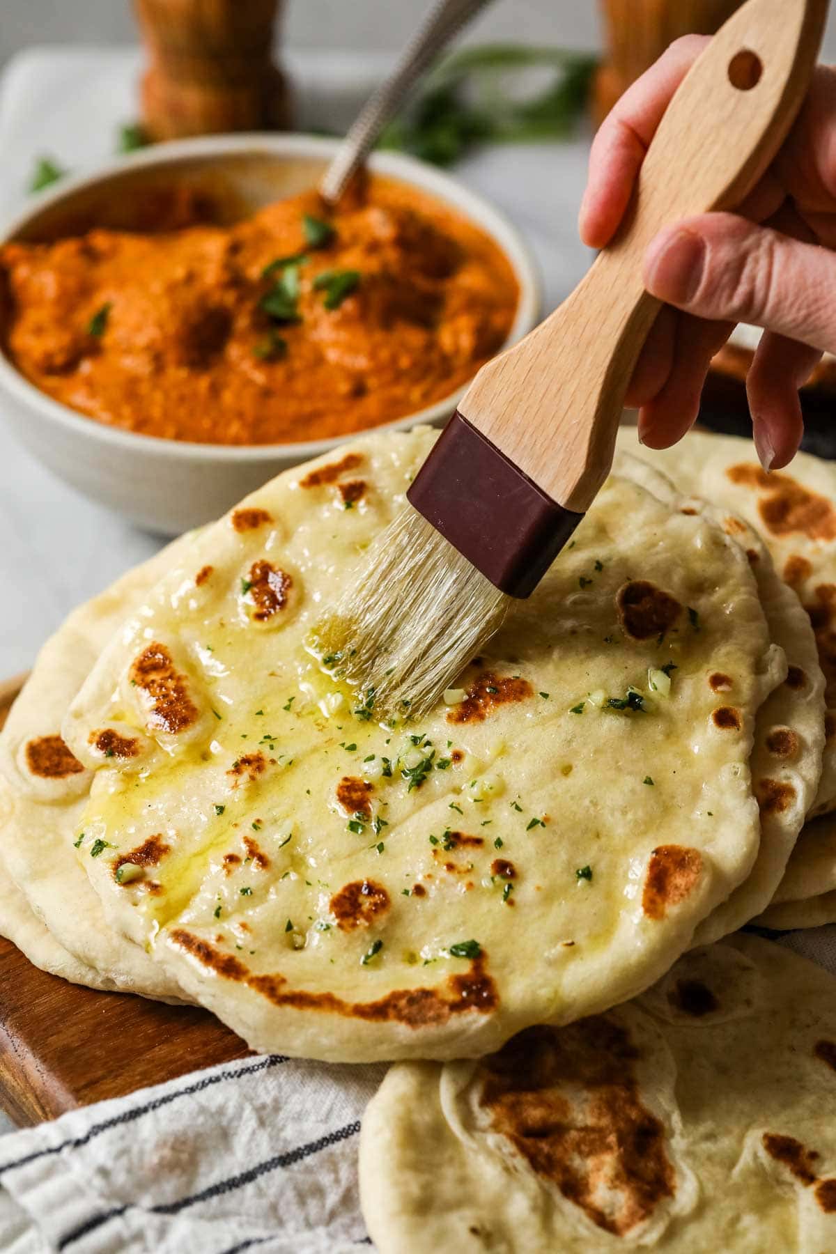 Garlic butter being spread onto garlic naan with a pastry brush.