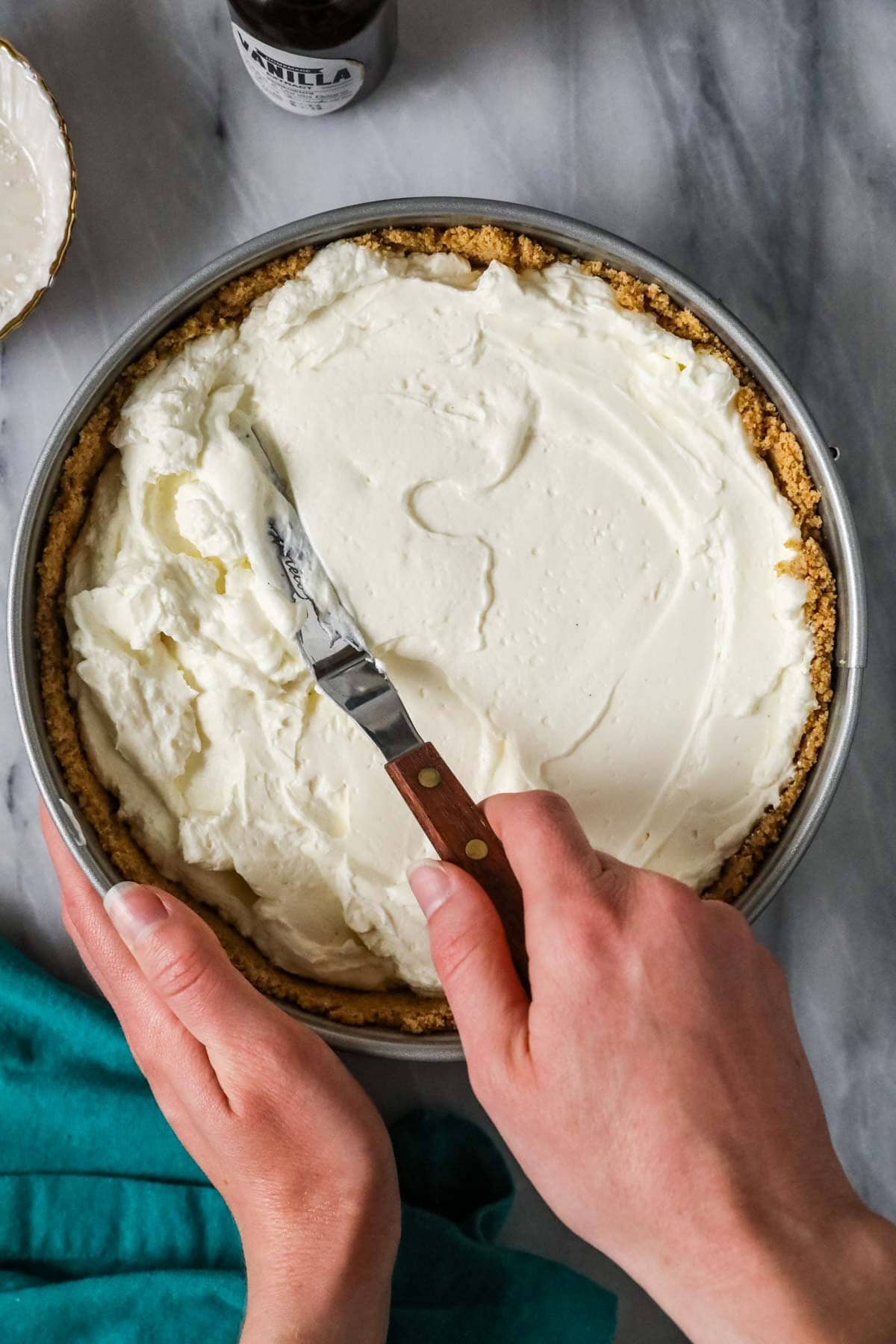 Offset spatula spreading cheesecake batter into a springform pan.