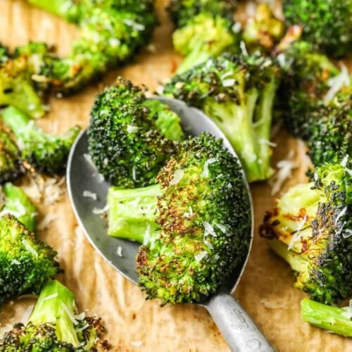 Spoonful of roasted broccoli being scooped off a baking sheet.