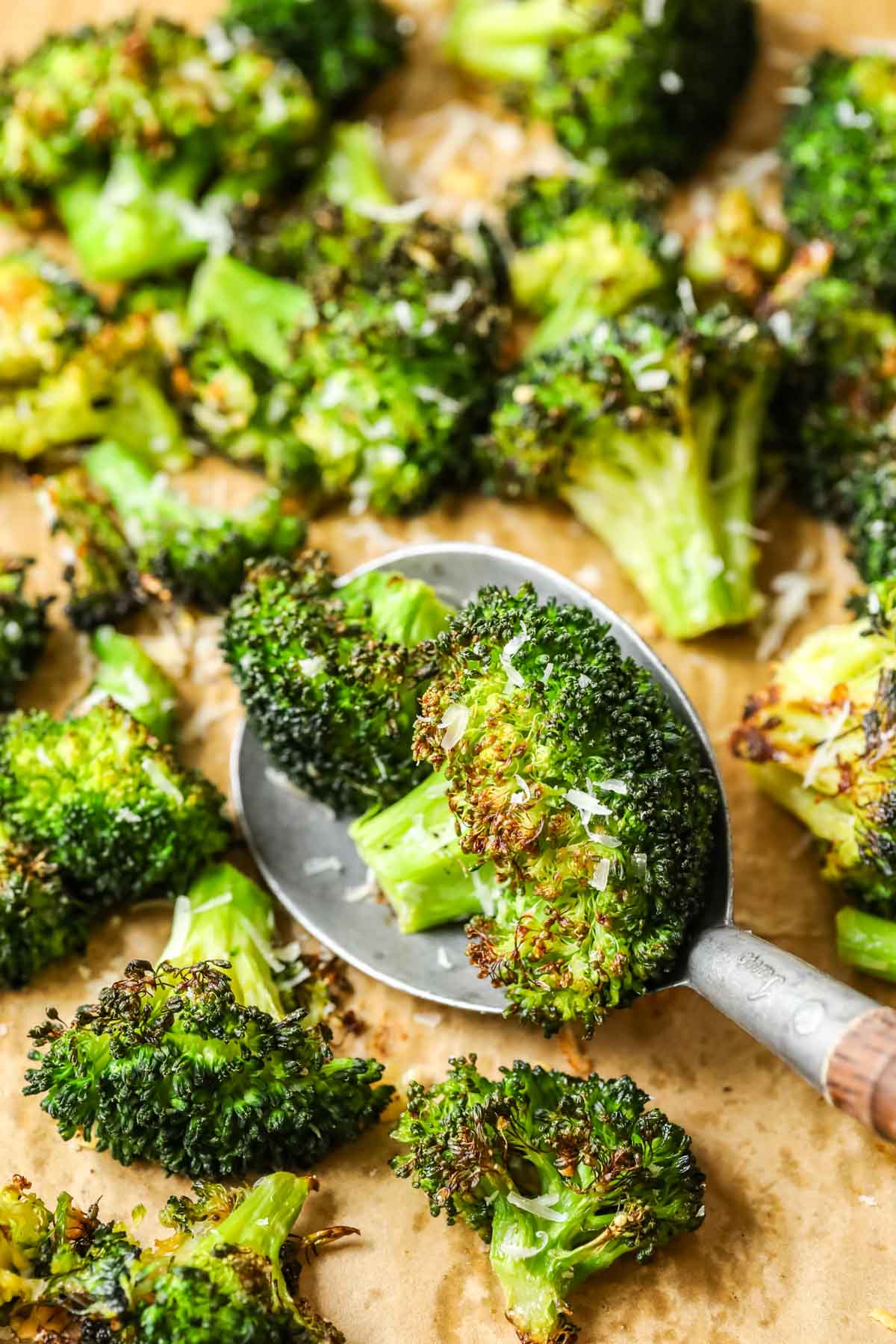 Spoonful of roasted broccoli being scooped off a baking sheet.
