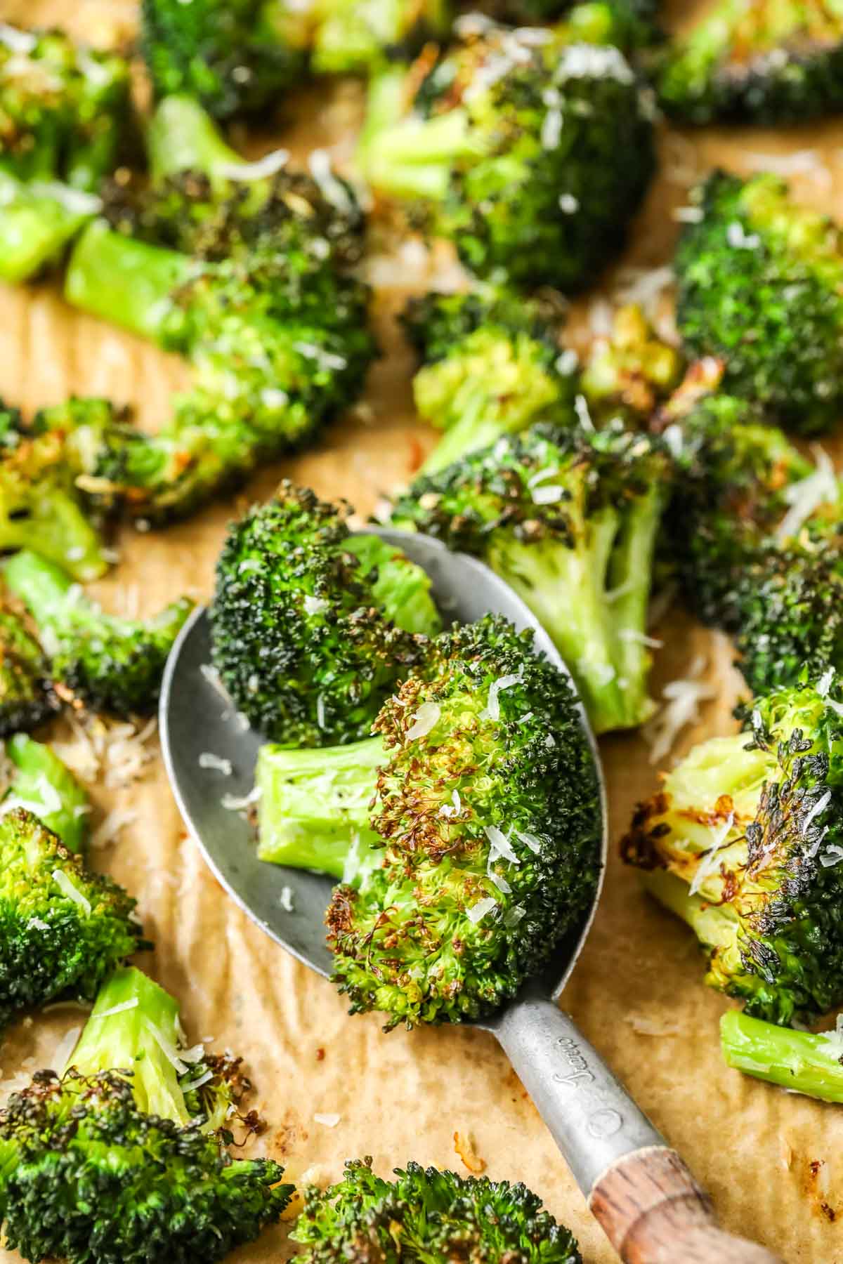 Spoonful of roasted broccoli being scooped off a baking sheet.