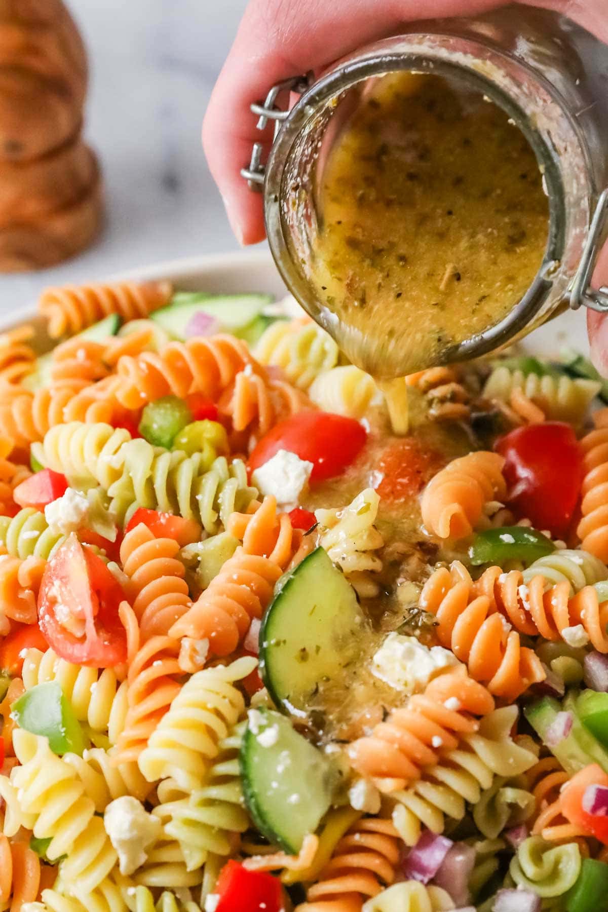 Pouring Italian dressing over pasta salad.