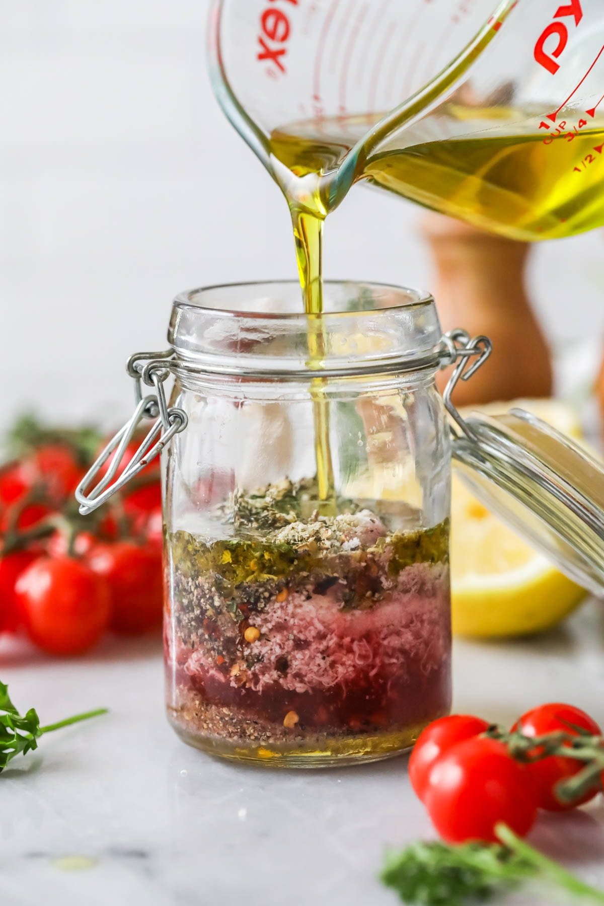 Olive oil being poured into a jar of spices, vinegar, dijon mustard, and more.