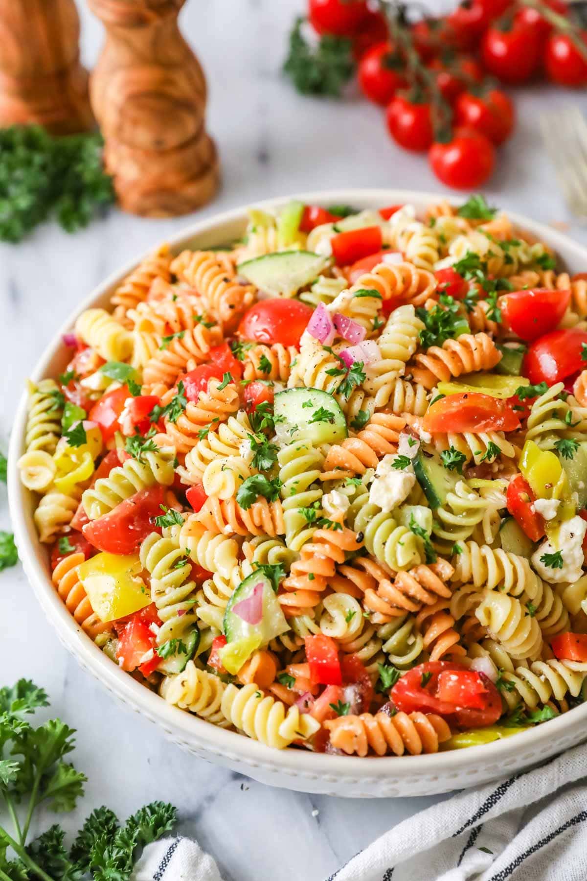 Bowl of pasta salad made with tri-color rotini, veggies, and feta cheese.