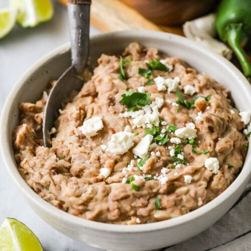 Bowl of homemade refried beans topped with cheese and cilantro.