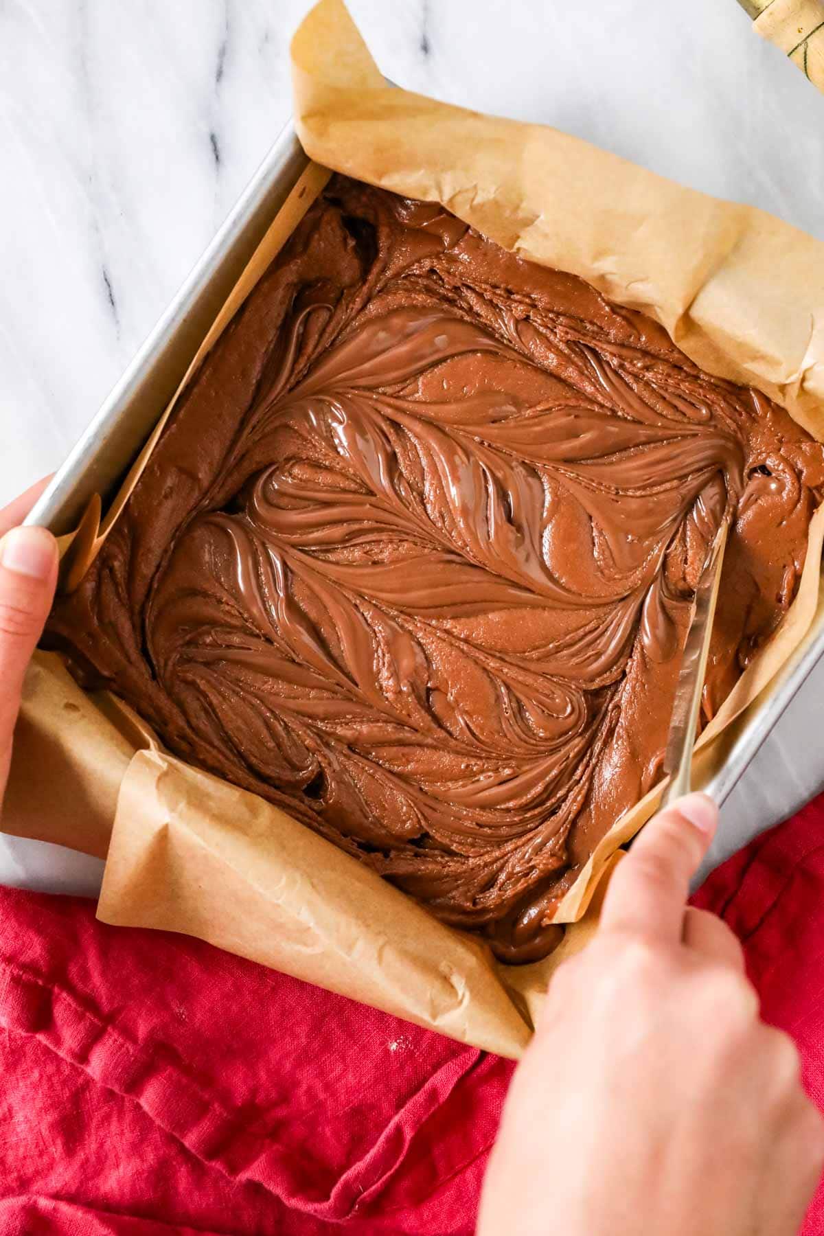 Overhead view of Nutella being swirled into a pan of brownie batter.
