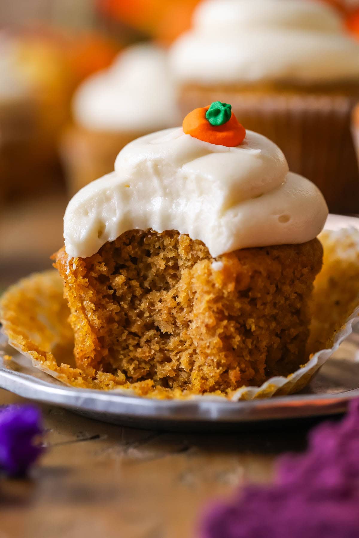 Bite missing from a pumpkin cupcake topped with cream cheese frosting and a pumpkin candy.