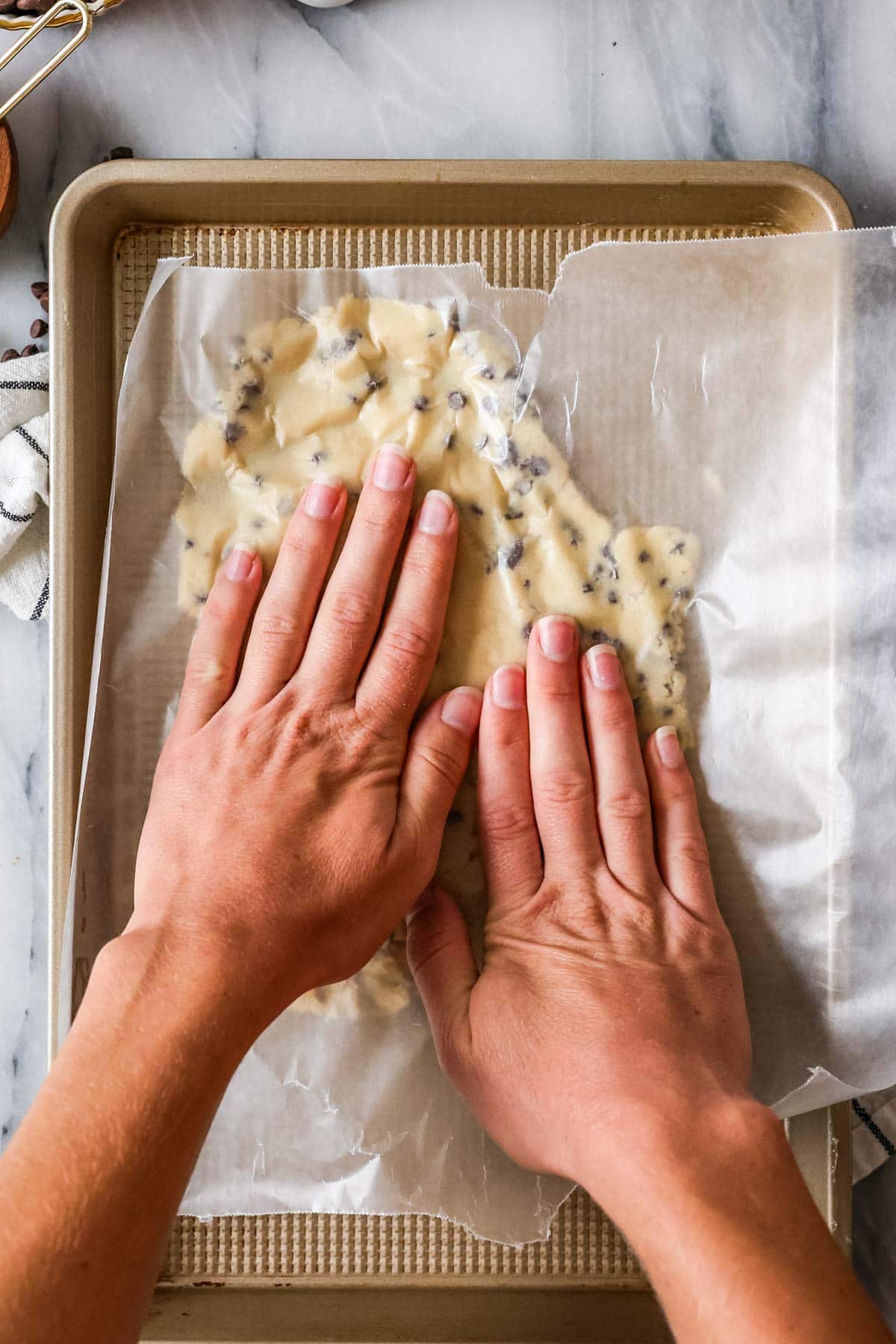 Hands pressing a thin cookie dough onto a cookie sheet.