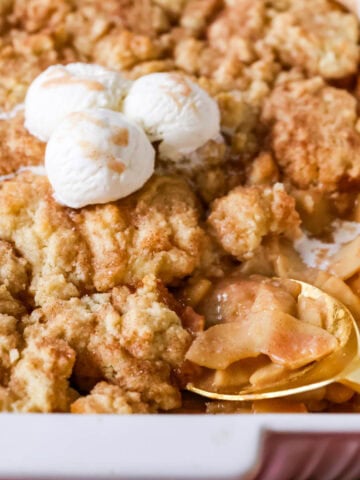 Spoon scooping a serving of apple cobbler from a baking dish.