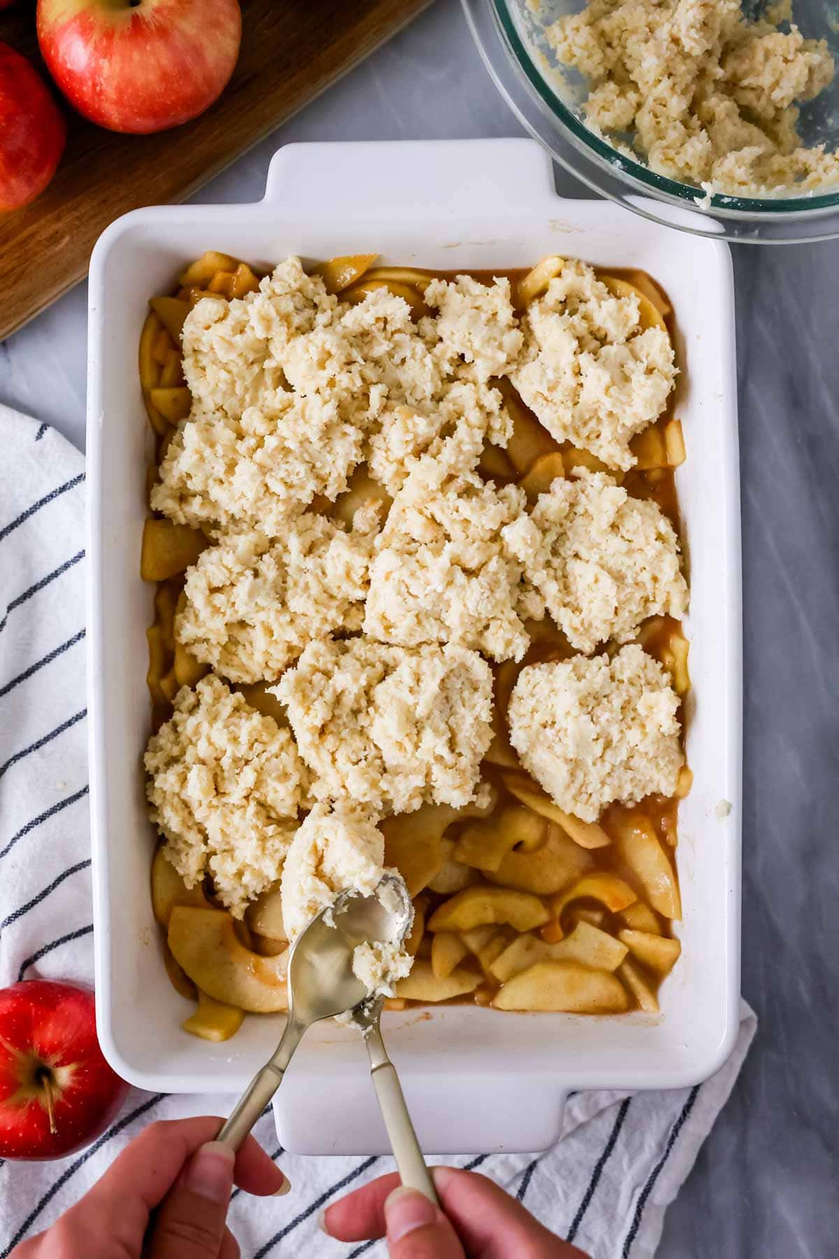 Overhead view of cobbler topping being dropped onto an apple filling.