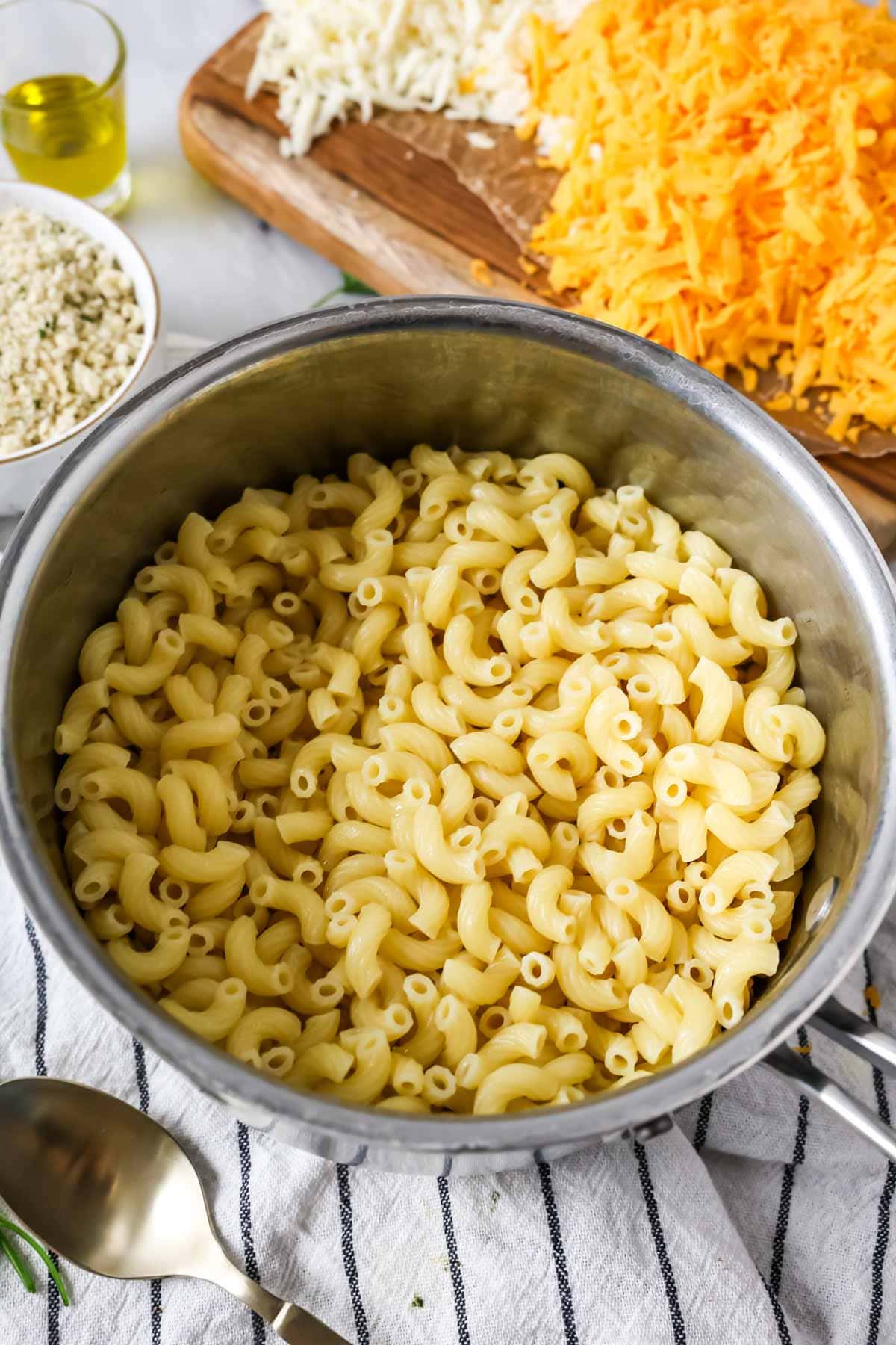 Boiled, drained pasta in a stainless steel colander with mac and cheese ingredients in background.