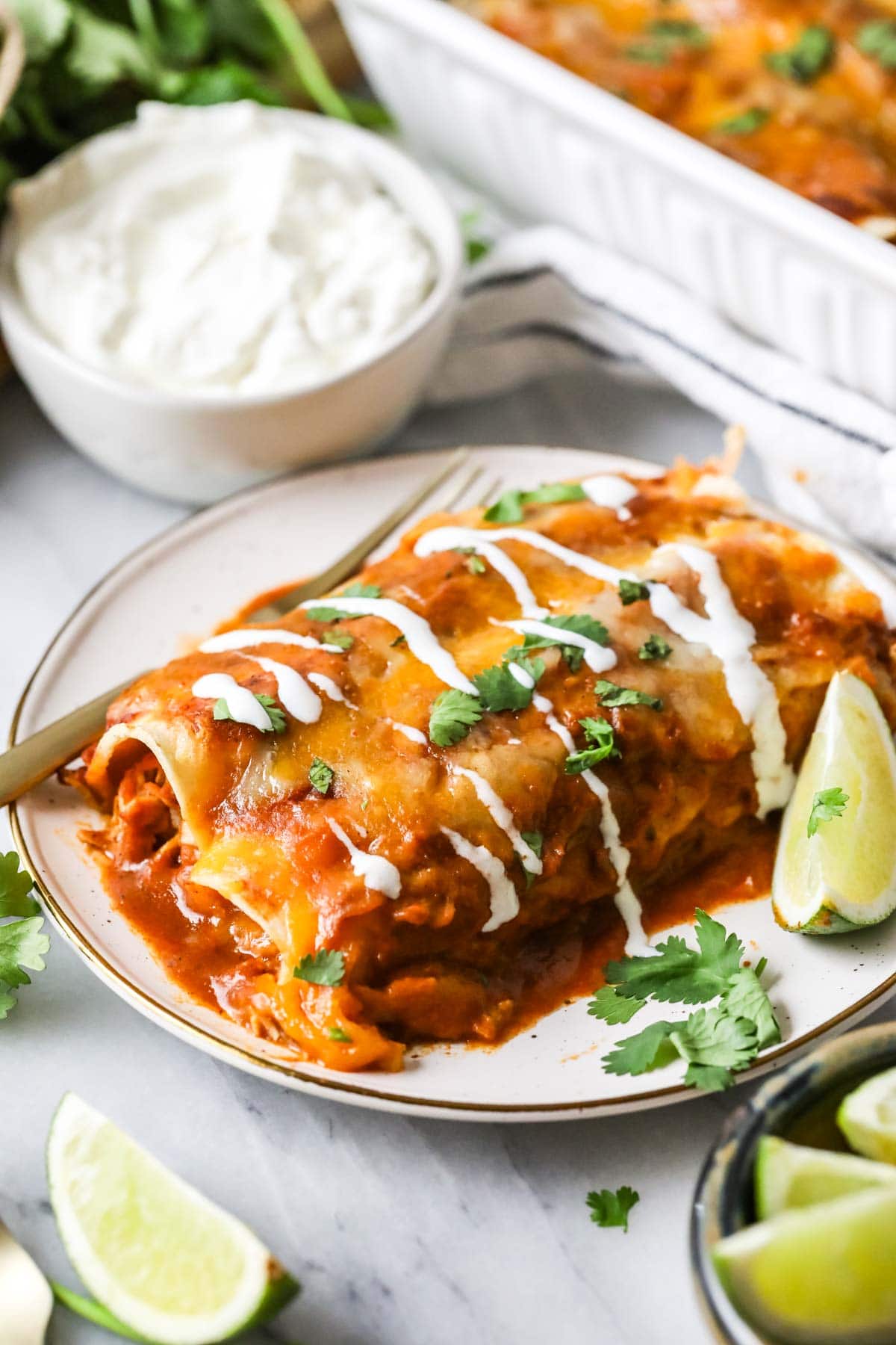 Two chicken enchiladas on a plate topped with sour cream and cilantro.