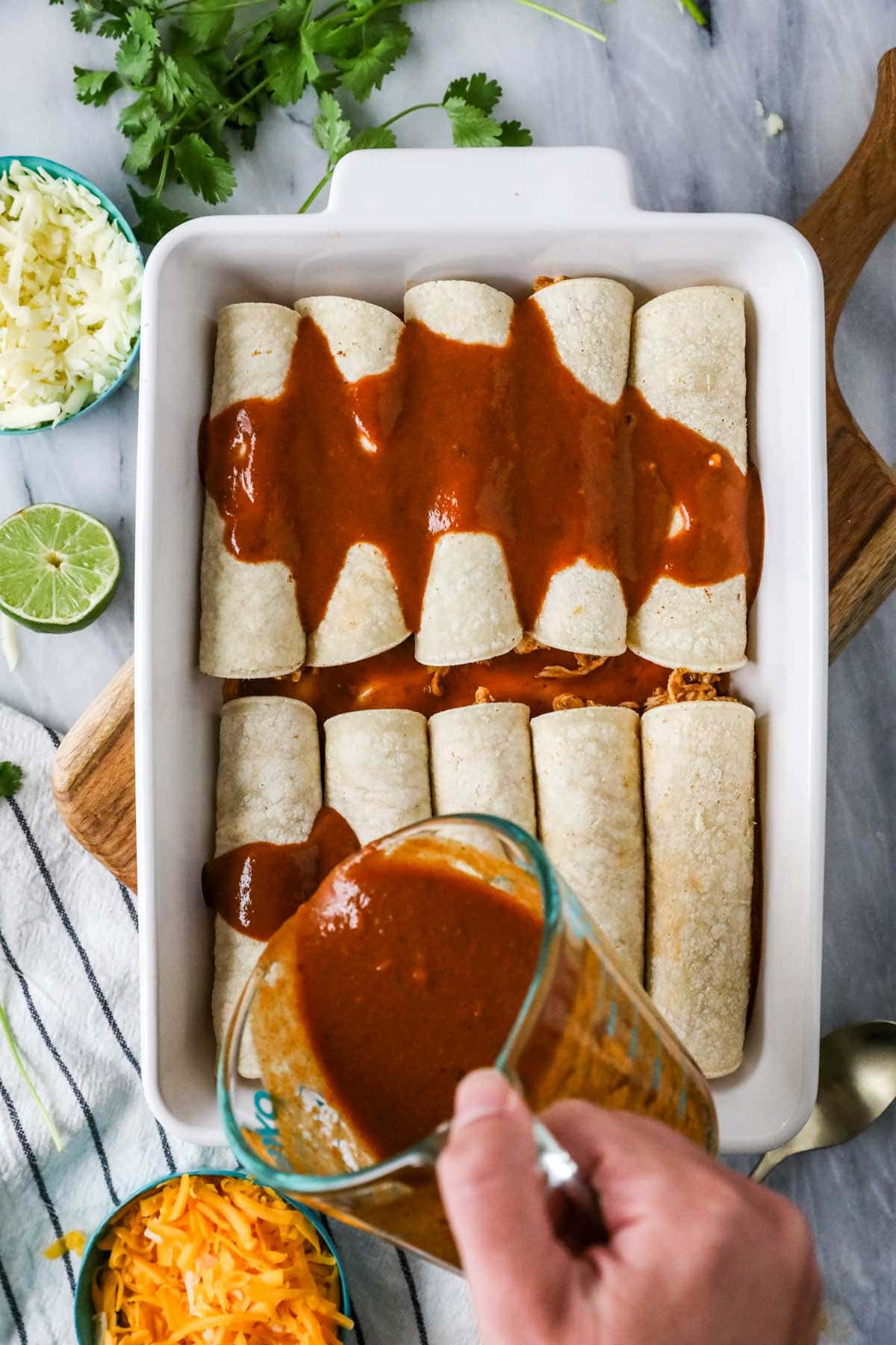 Overhead view of enchilada sauce being poured over tortillas that have been stuffed with thicken and cheese.