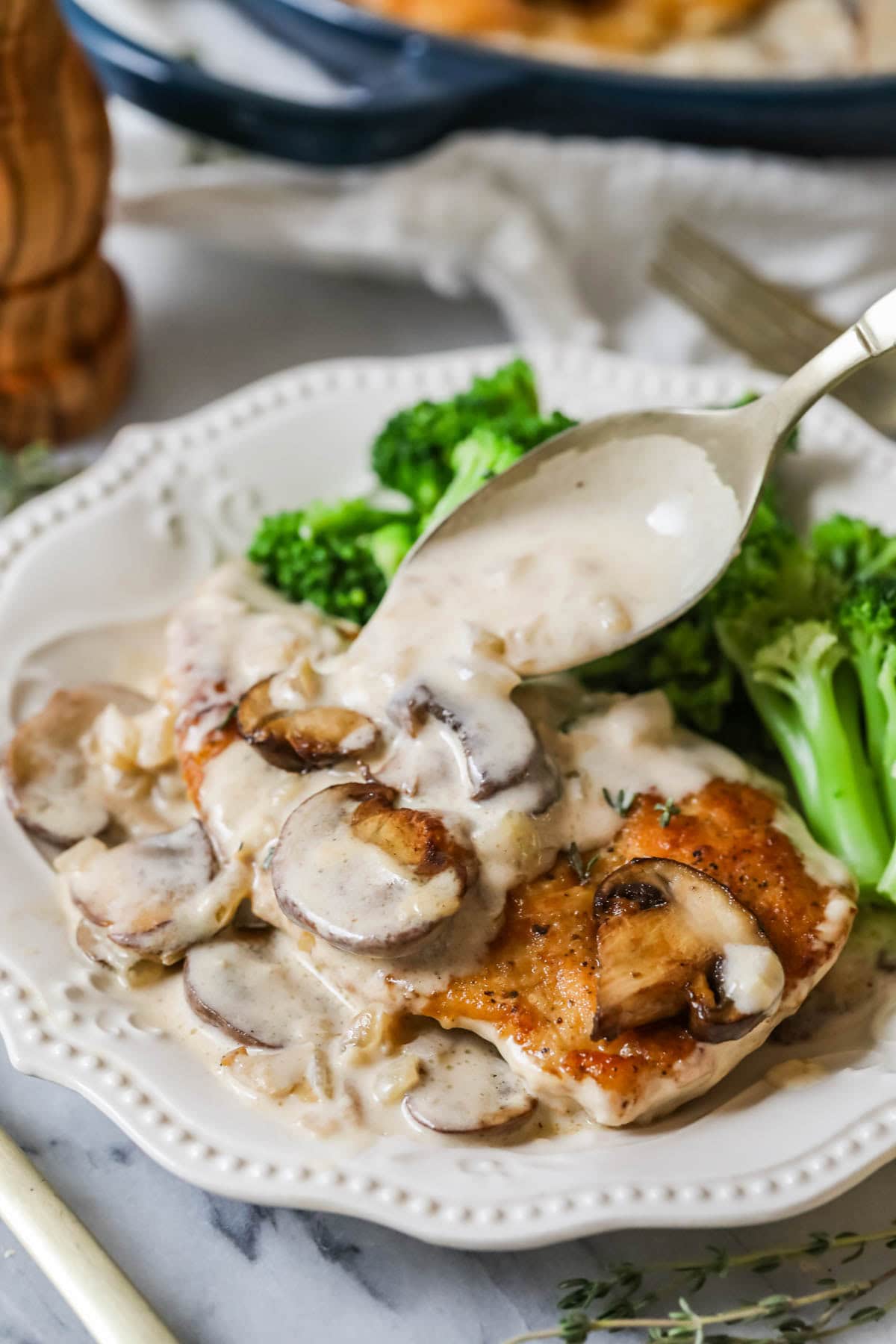 Creamy mushroom sauce being spooned over a chicken cutlet on a plate with broccoli.