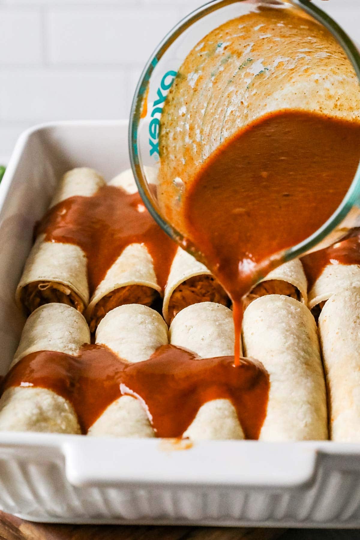 Sauce being poured over enchiladas.