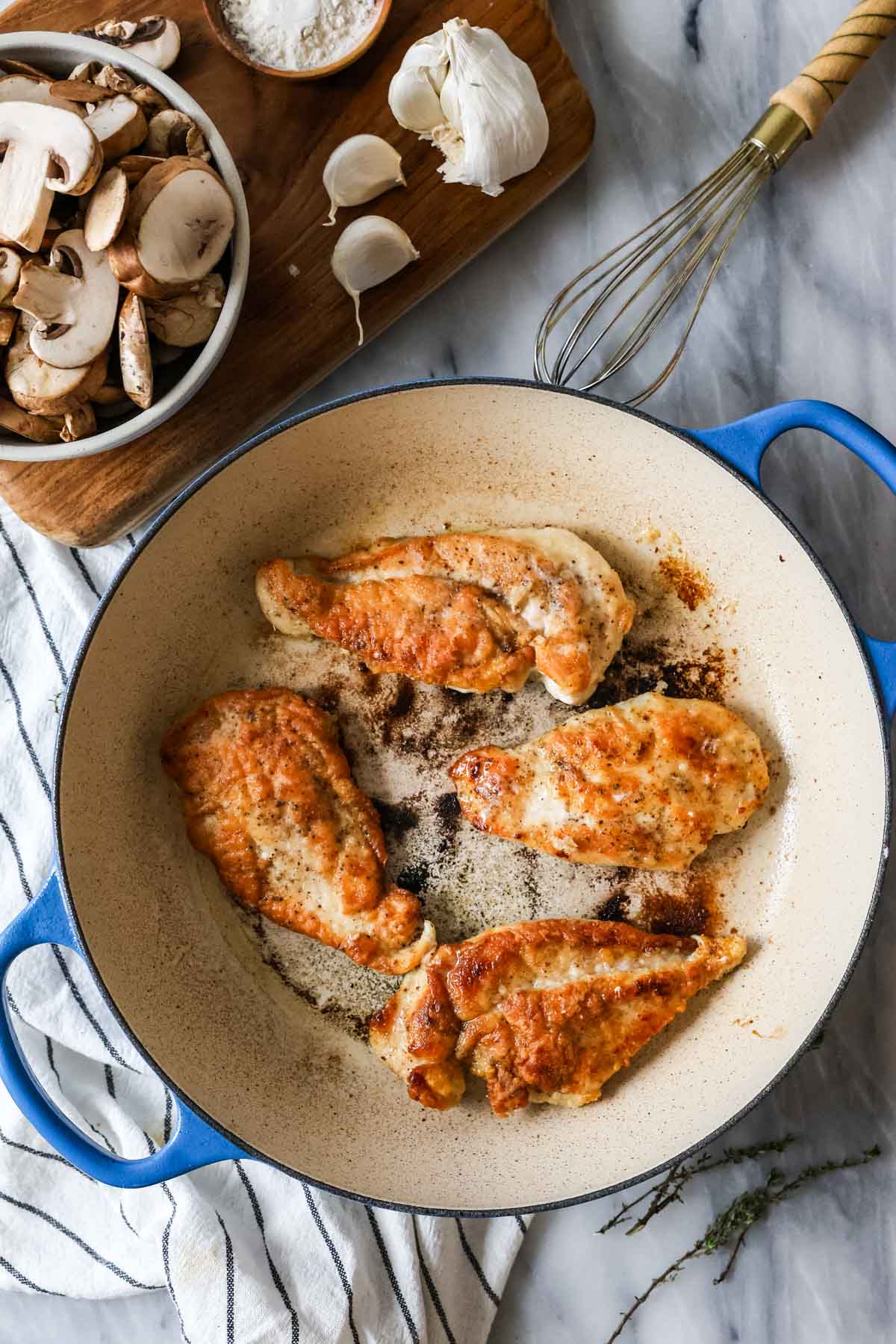 Overhead view of chicken cutlets searing in a skillet.