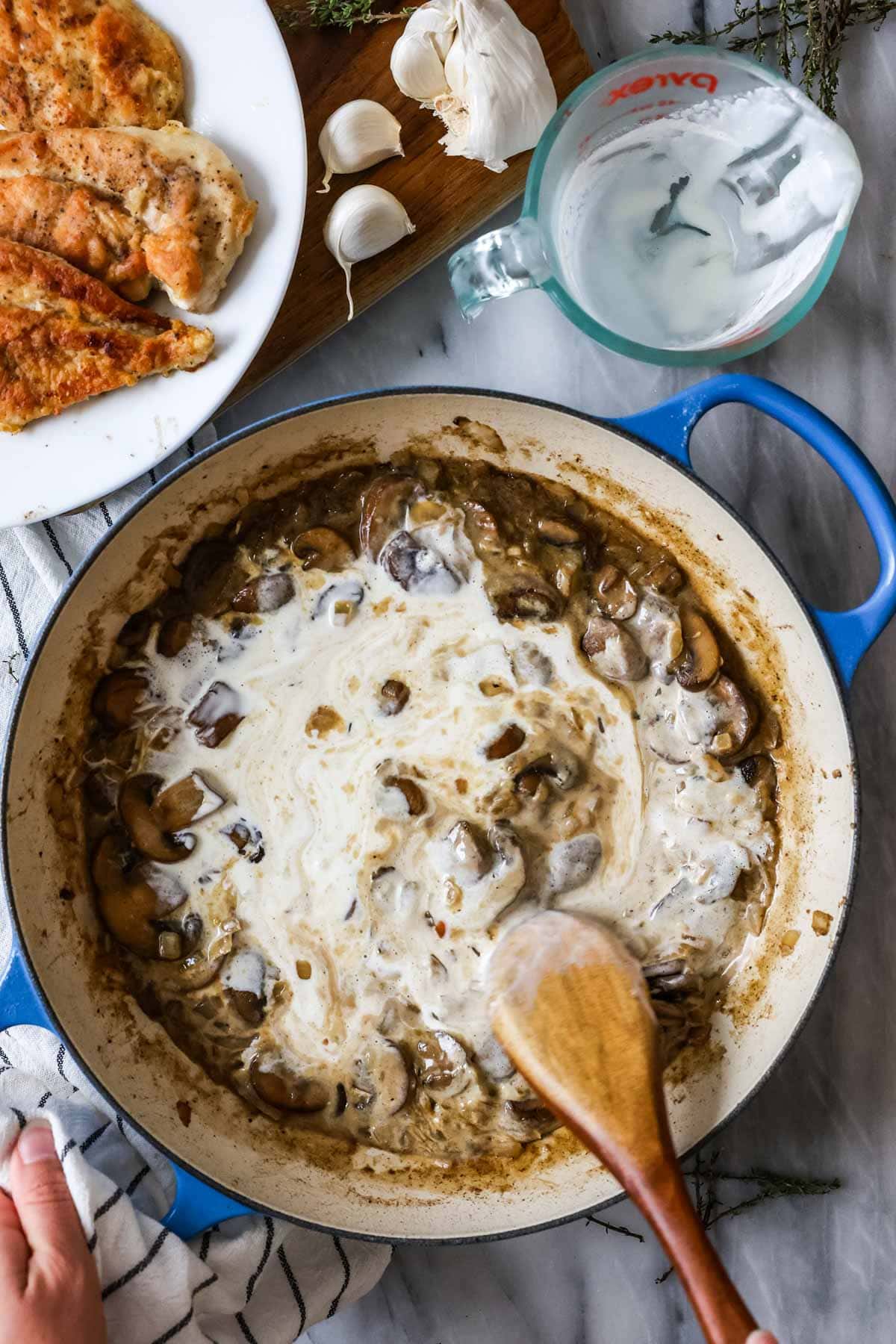 Cream being stirred into sauteed mushrooms in a skillet.