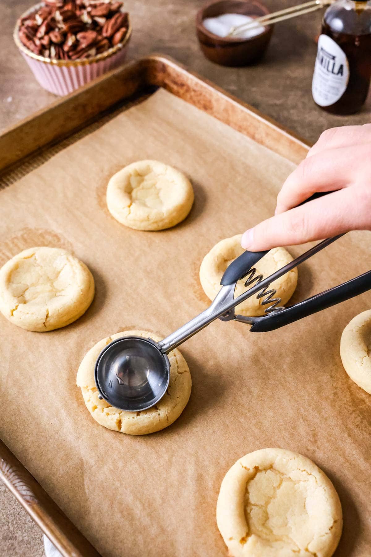 Indents being made in cookies so a pecan filling can go in.