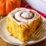 Pumpkin cinnamon roll frosted with cream cheese icing on a plate.