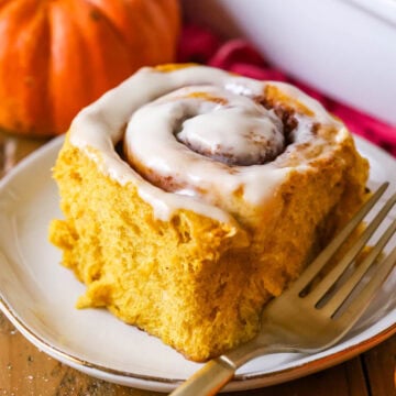 Pumpkin cinnamon roll frosted with cream cheese icing on a plate.