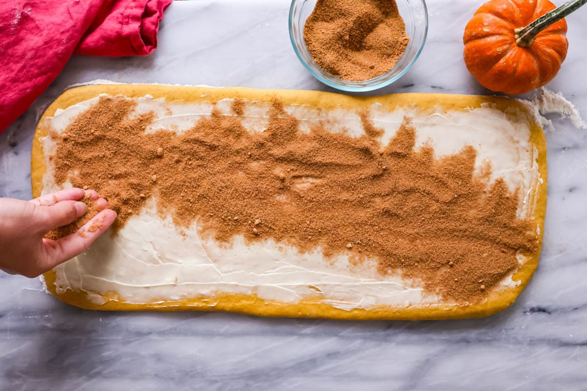 Cinnamon and sugar being sprinkled over a rectangle of pumpkin dough.
