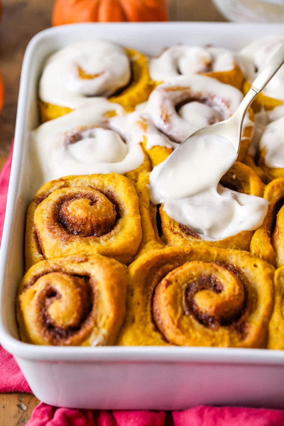 Frosting being spread over pumpkin cinnamon rolls.
