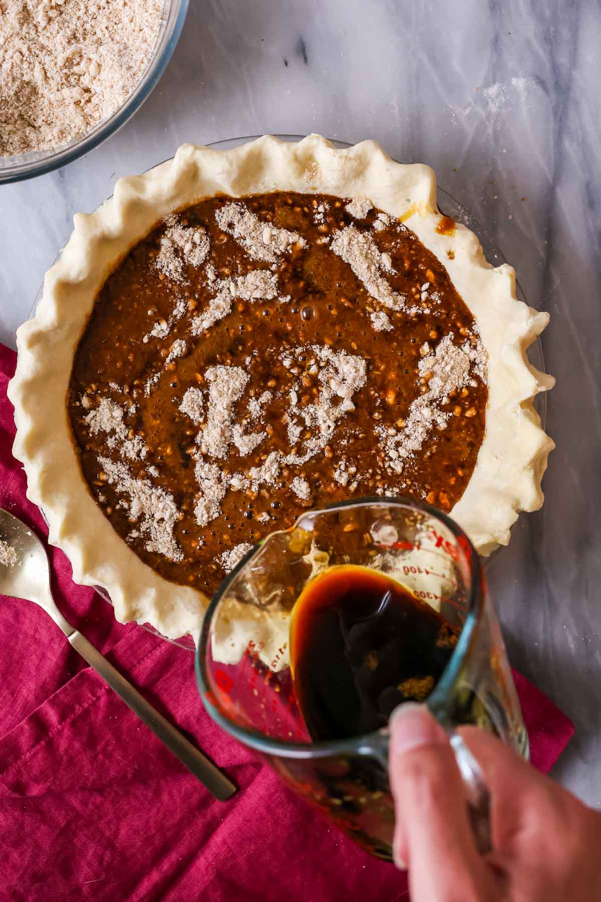 Overhead view of a molasses mixture being poured over a crumb layer in a pie crust.