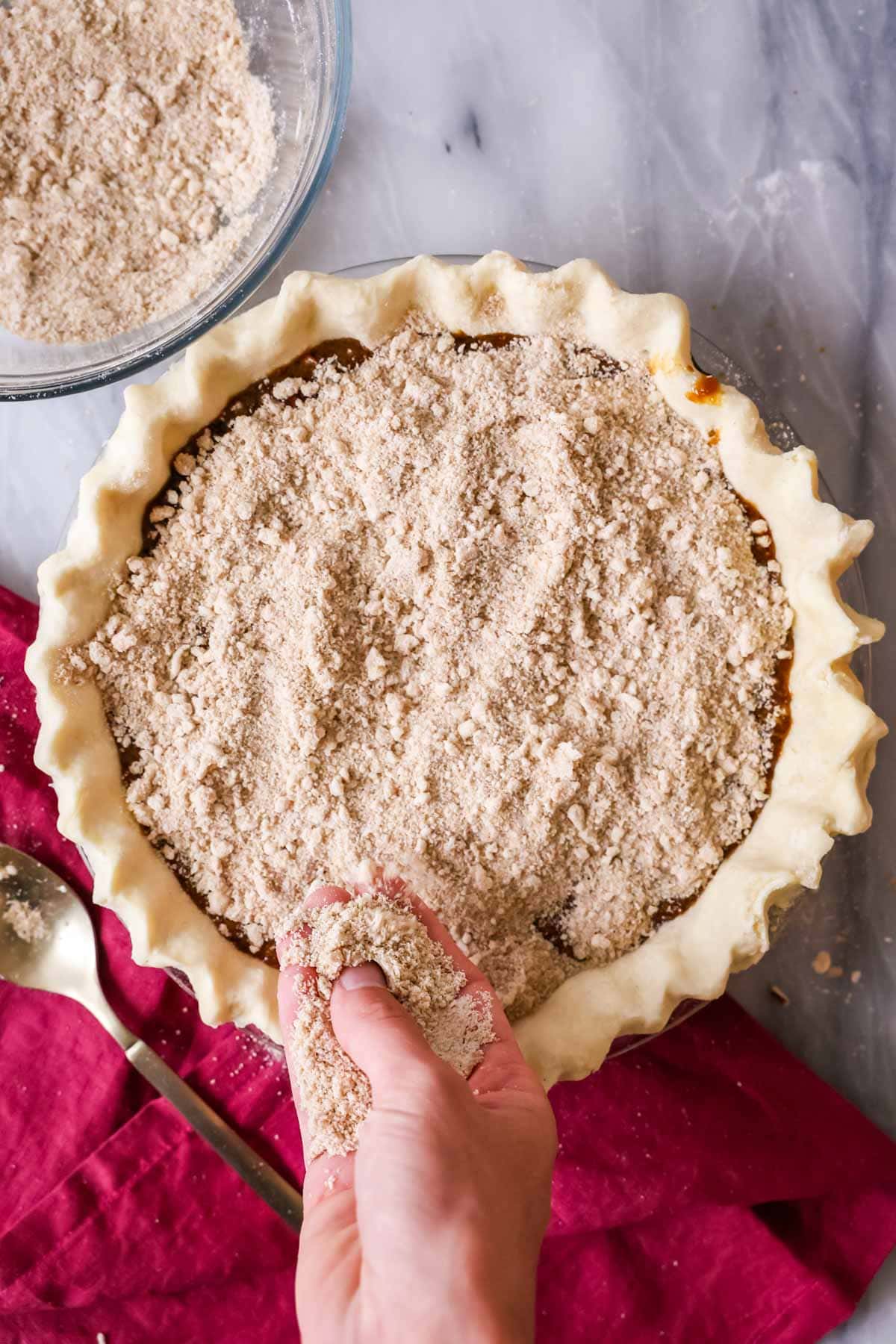 Overhead view of a crumb layer being sprinkled over a pie crust.