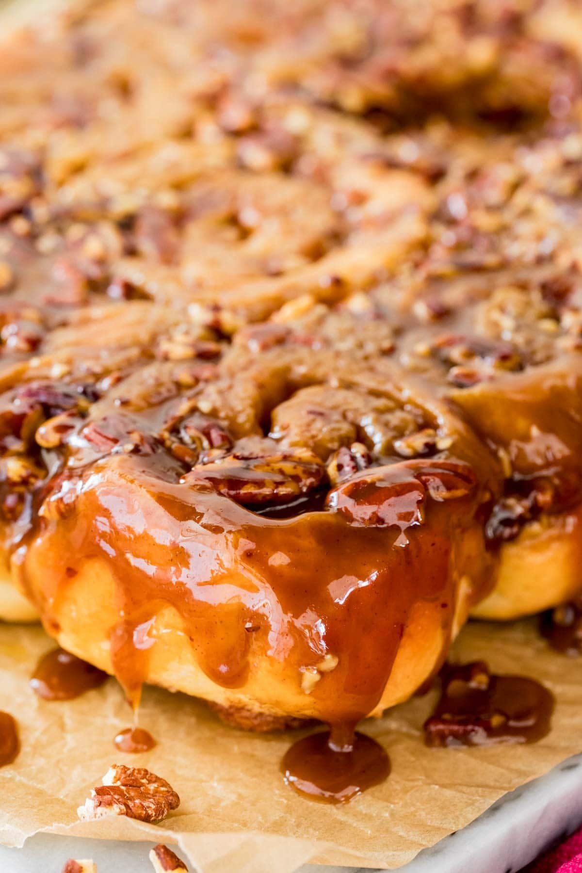Close up of a sticky bun, glaze dripping off edge, gooey pecans on top.